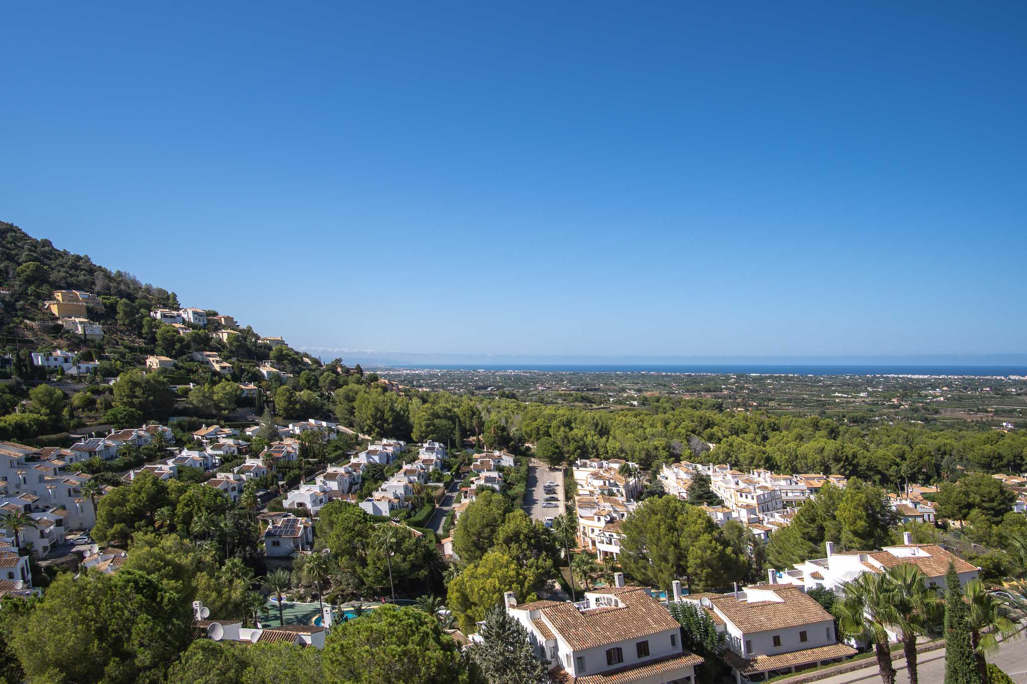 Vistas panorámicas desde La Sella hacia el mar Mediterráneo, mostrando la arquitectura residencial integrada en un entorno de frondosa vegetación y cielos despejados.