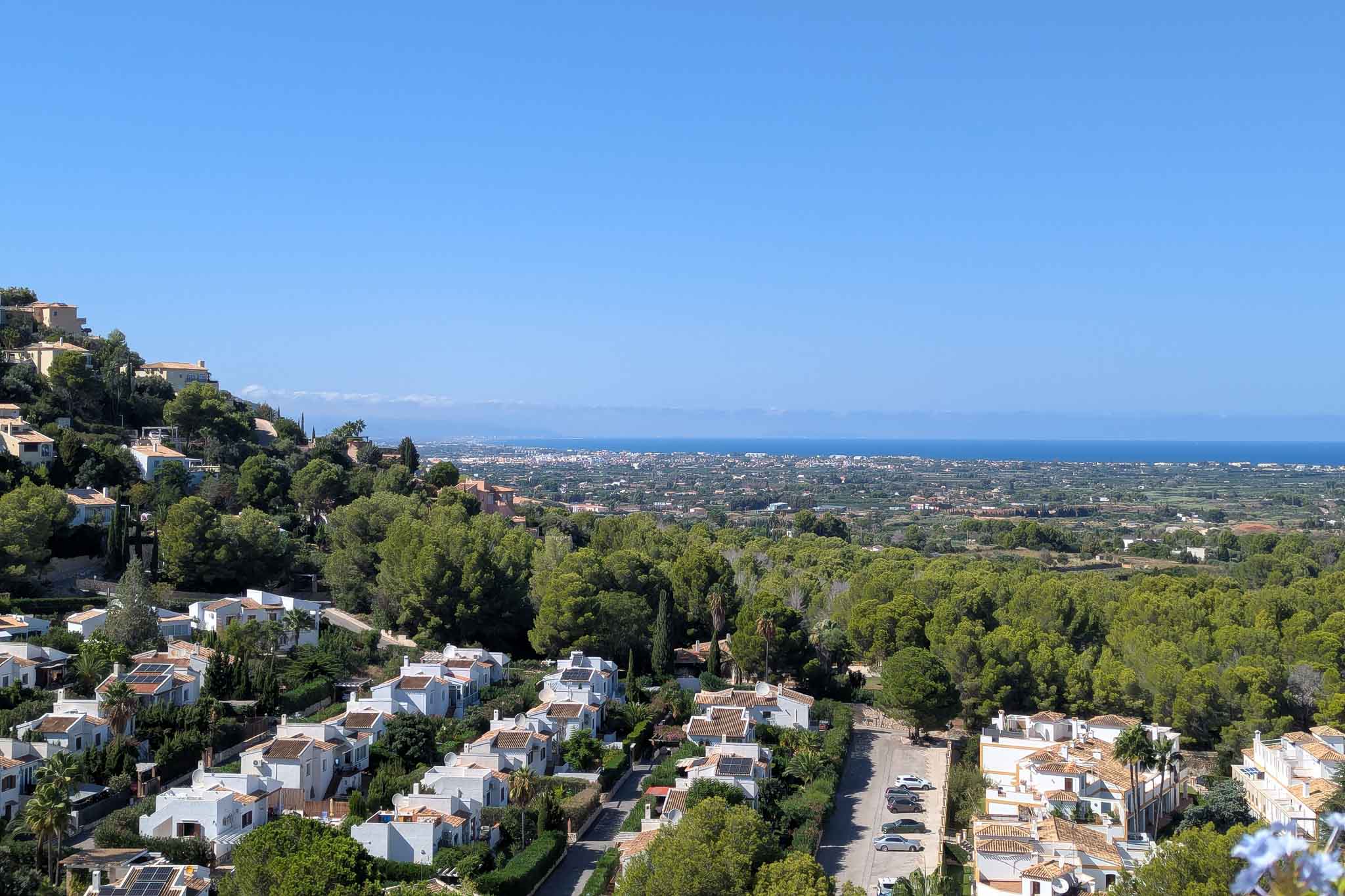 Vistas panorámicas desde La Sella hacia la costa de Dénia, mostrando la integración de las villas blancas entre el denso bosque de pinos y el mar Mediterráneo al fondo.