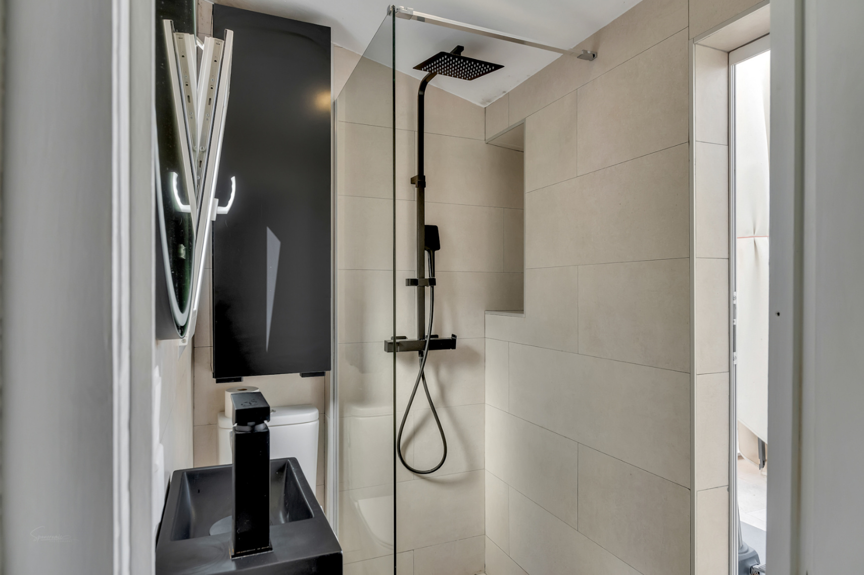 Detalle de baño moderno con ducha de efecto lluvia negra, lavabo negro y azulejos color crema.