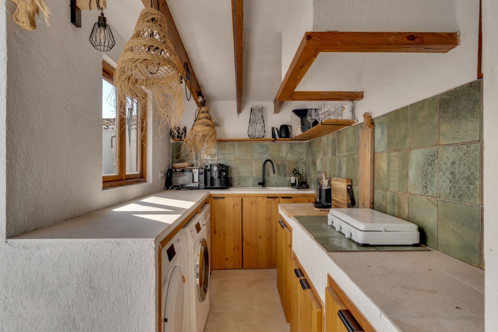 Detalle de la cocina con muebles de madera clara, encimera de obra y azulejos verdes.
