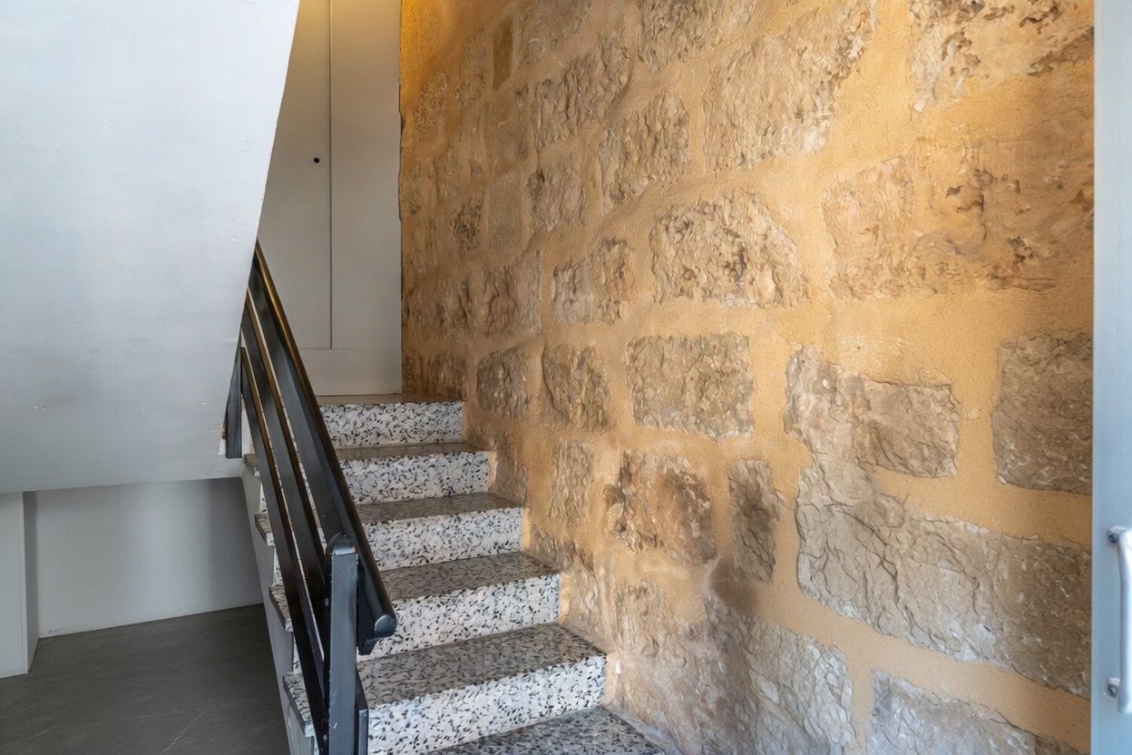 Detalle de la escalera con pared de piedra vista y peldaños de terrazo.