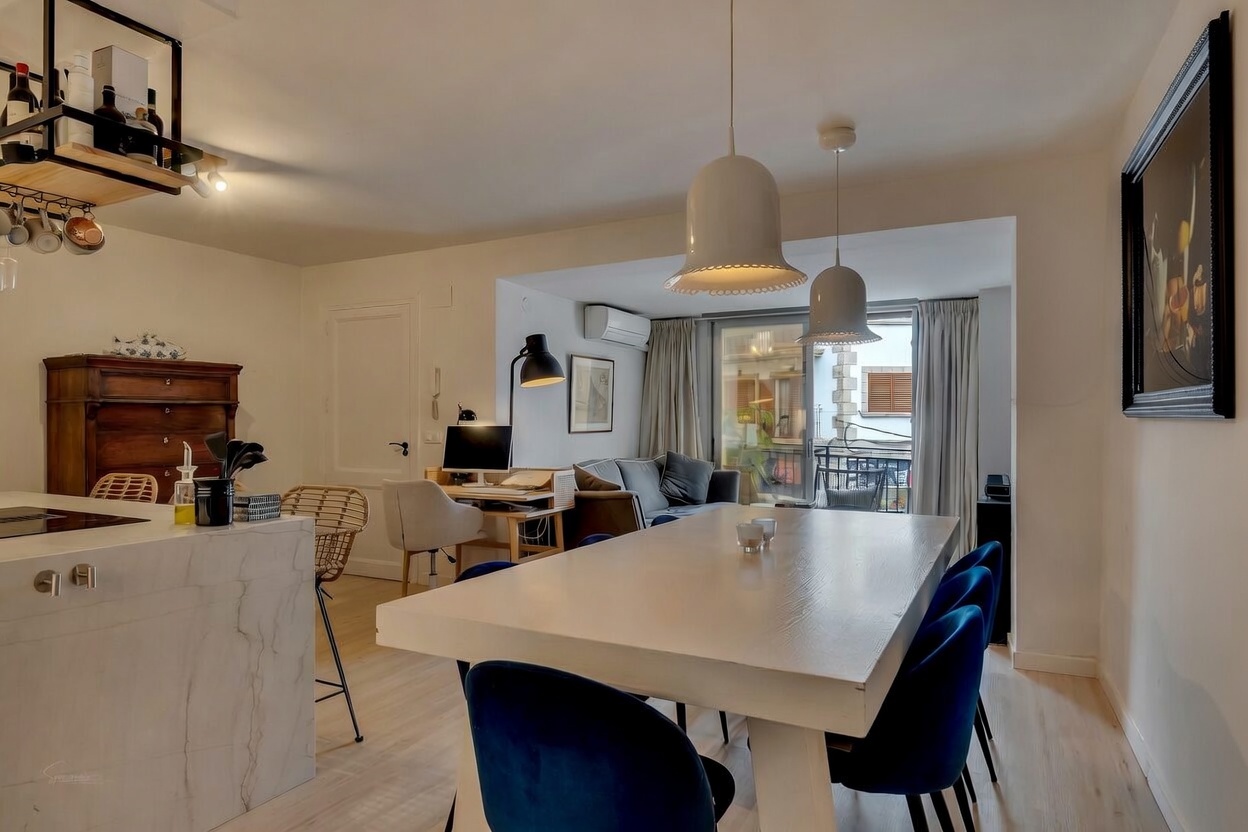 Detalle del salón-comedor con mesa blanca y sillas azules, iluminación moderna y acceso al balcón.