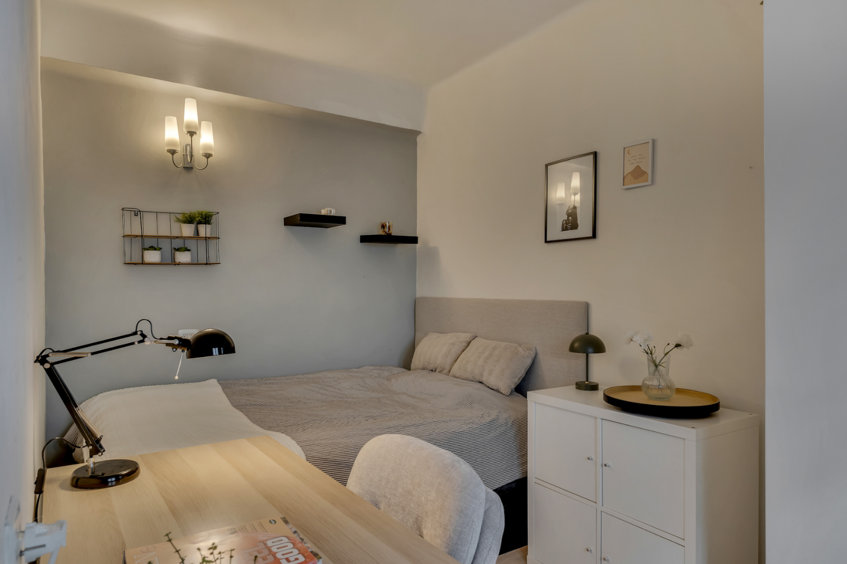 Dormitorio luminoso con escritorio de madera clara y estanterías decorativas.