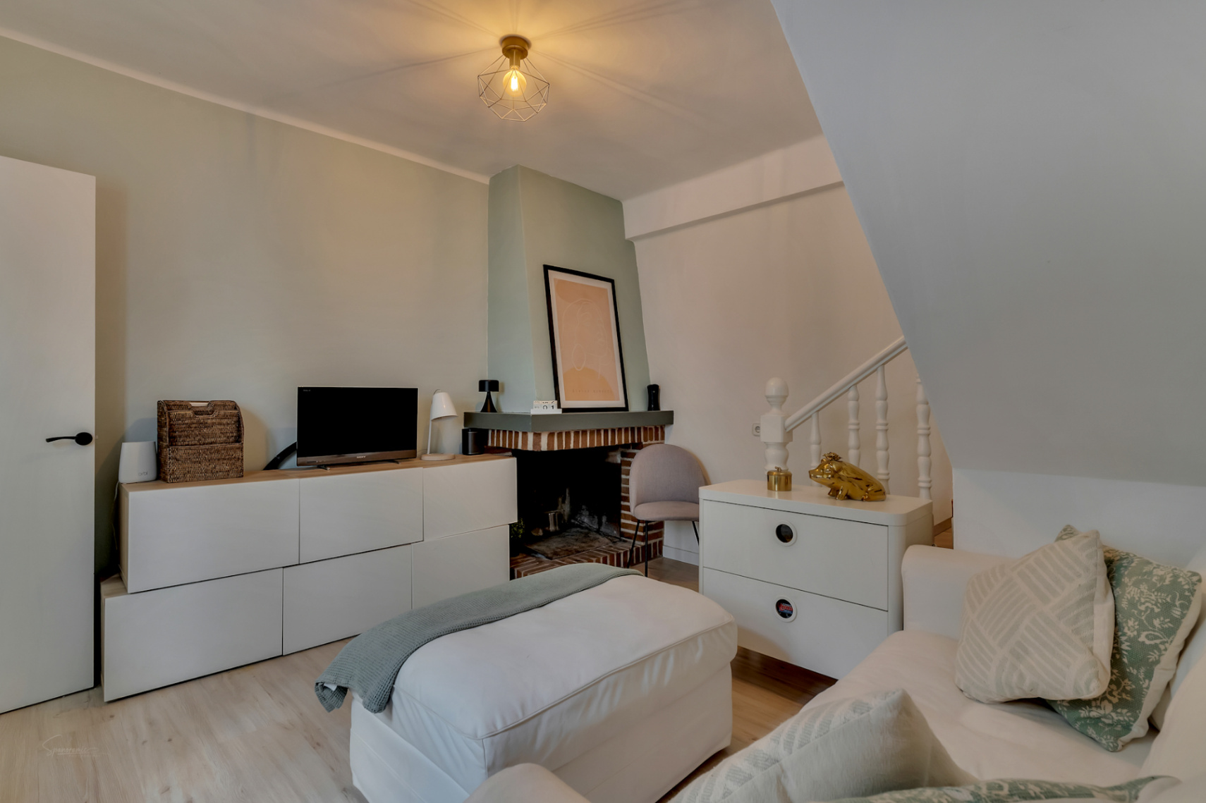 Salón con chimenea de ladrillo, muebles blancos y suelo de madera clara.