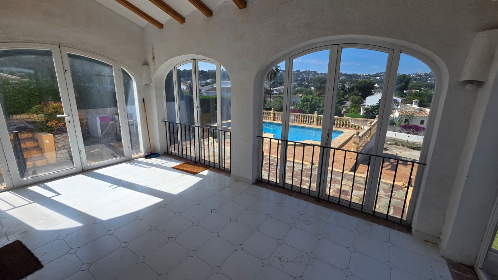 Naya acristalada con ventanales en arco, suelo de baldosa blanca y vigas de madera vistas, con vistas directas a la piscina y al entorno de El Tosalet.