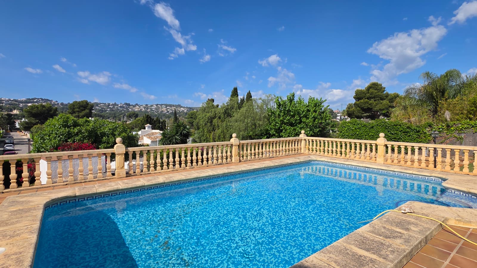 Piscina elevada revestida con mosaico azul, rodeada por una balaustrada de piedra tradicional con vistas despejadas hacia el entorno natural de Jávea.