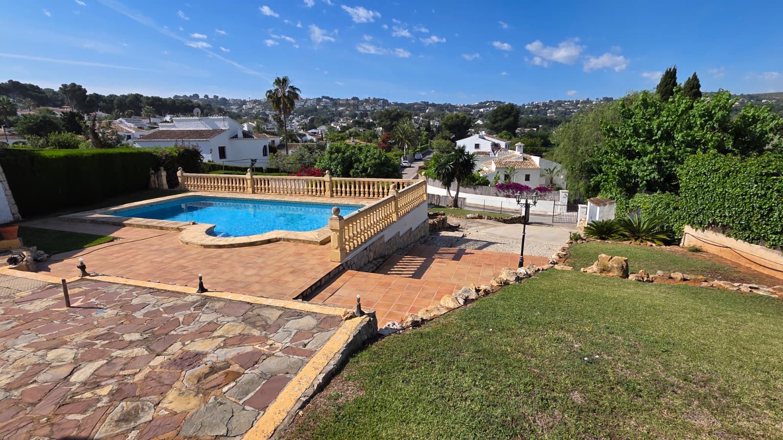 Piscina exterior con balaustrada clásica y terraza de terracota, rodeada de zonas verdes y vistas despejadas al valle de Jávea.