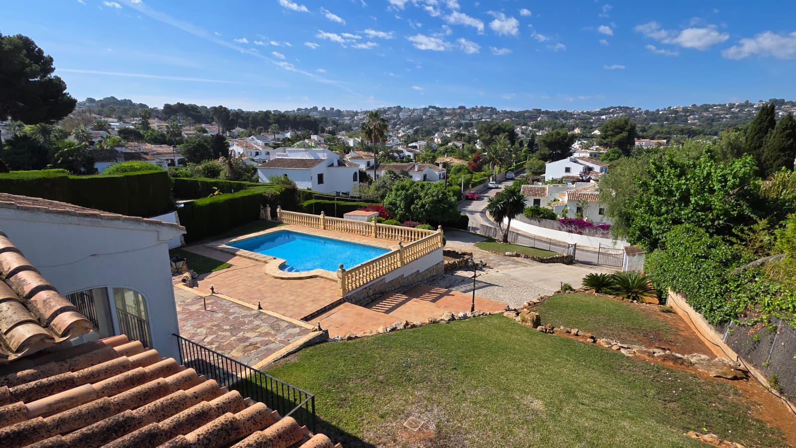 Vista elevada de la piscina privada con balaustrada de piedra, terraza de terracota y zona de césped, con vistas despejadas a la urbanización El Tosalet.