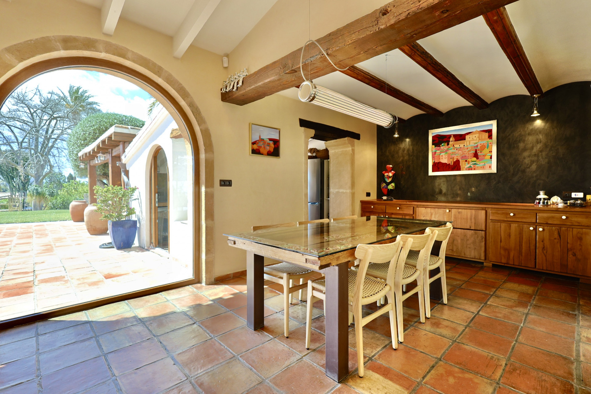 Comedor rústico con suelo de terracota, mesa de madera y acceso al jardín a través de un arco de piedra.