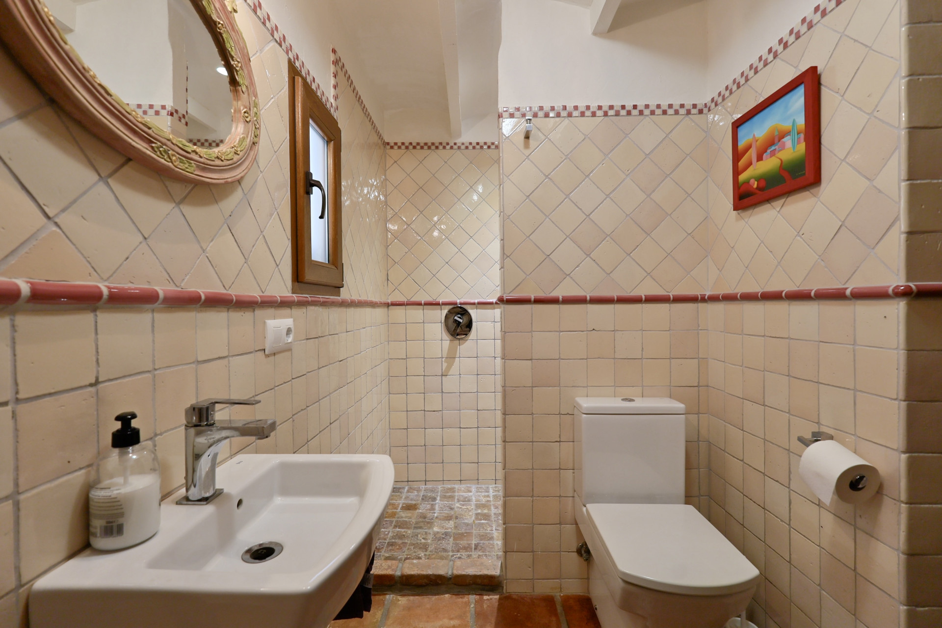 Detalle de baño con azulejos color crema, espejo ovalado y lavabo blanco en Villa en Jávea.
