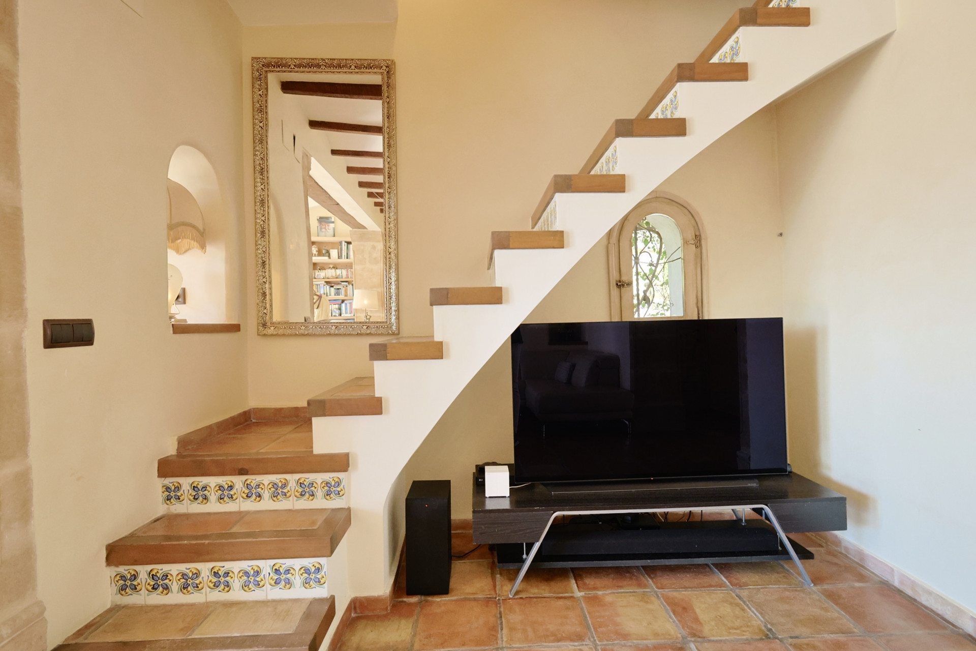Detalle de escalera con azulejos decorativos y TV en salón con suelo de terracota.