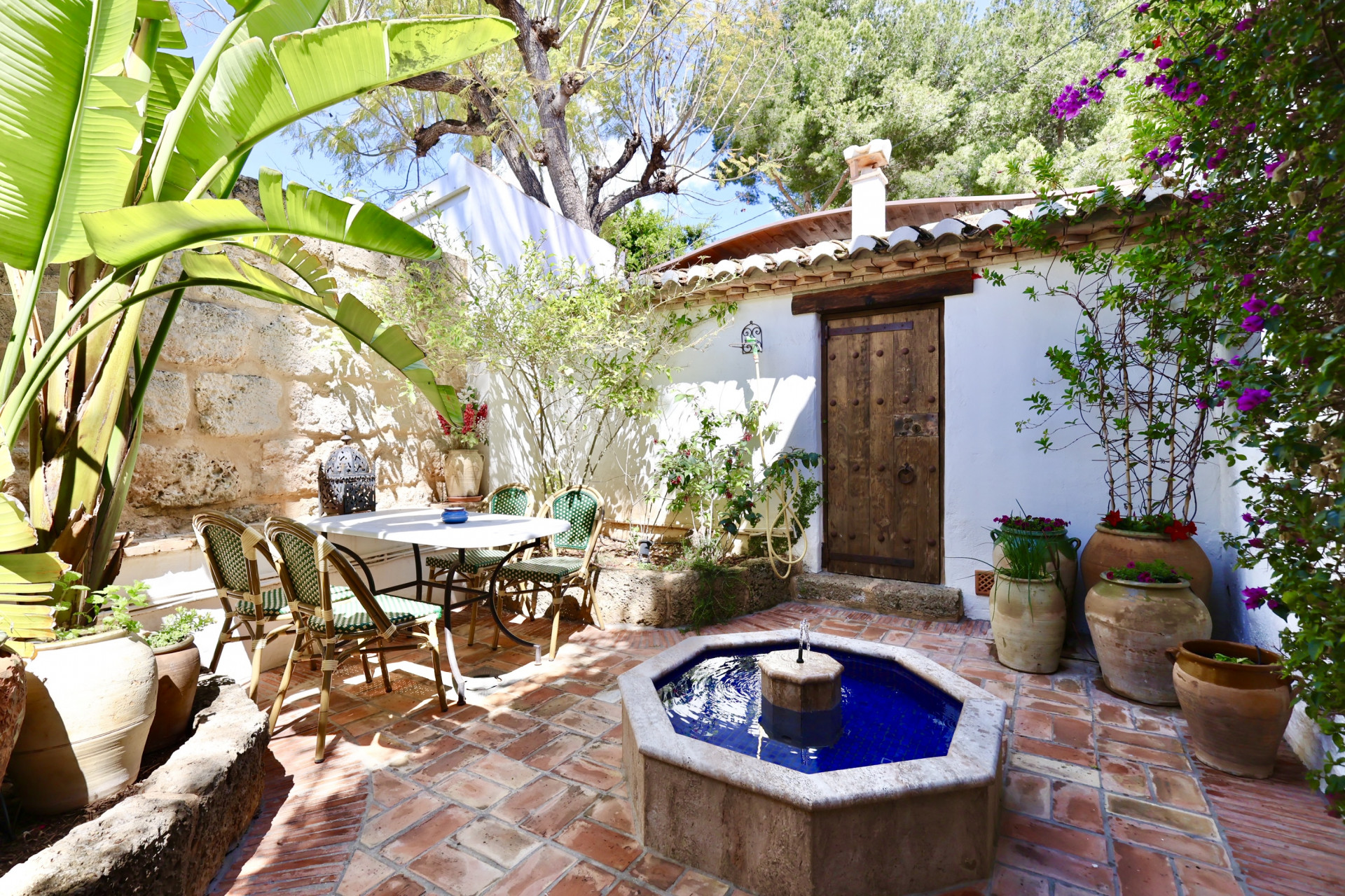Patio con fuente octogonal de mosaico azul y comedor exterior con suelo de terracota.