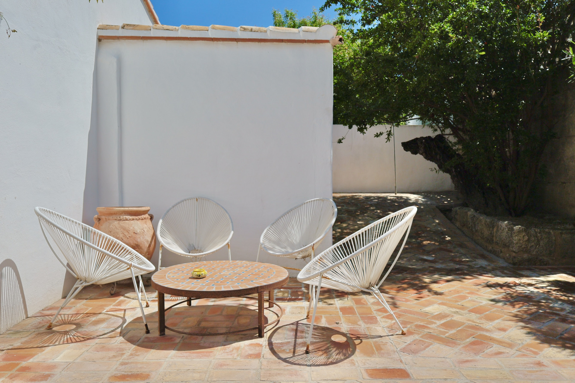 Patio con suelo de terracota, sillas de cuerda blanca y mesa de mosaico, ideal para relajarse al aire libre.
