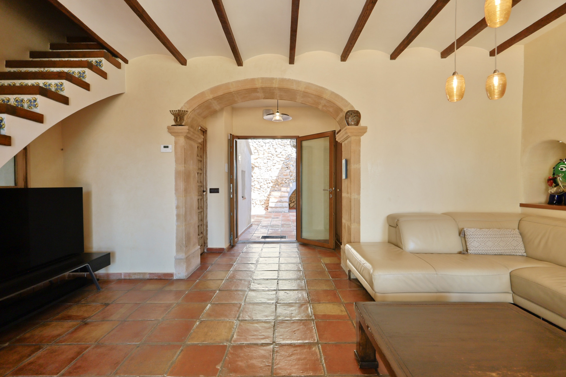 Salón con suelo de terracota, sofá de cuero y arco de piedra que da al exterior.