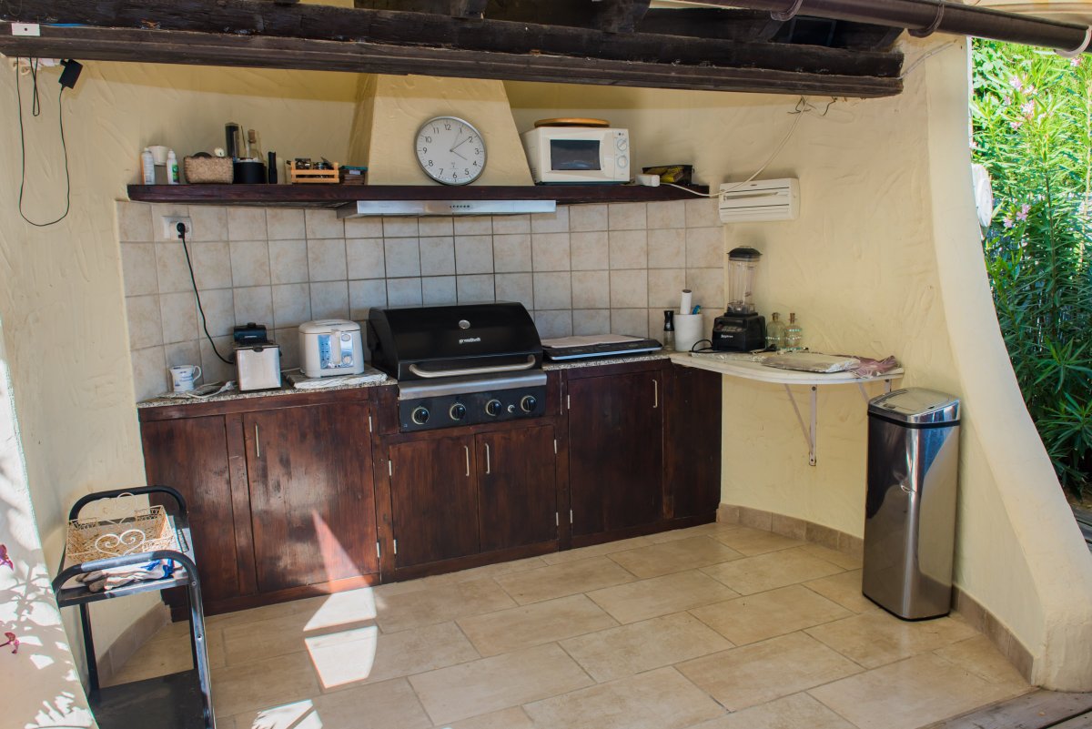 Cocina exterior equipada con parrilla, encimera de madera oscura y electrodomésticos.