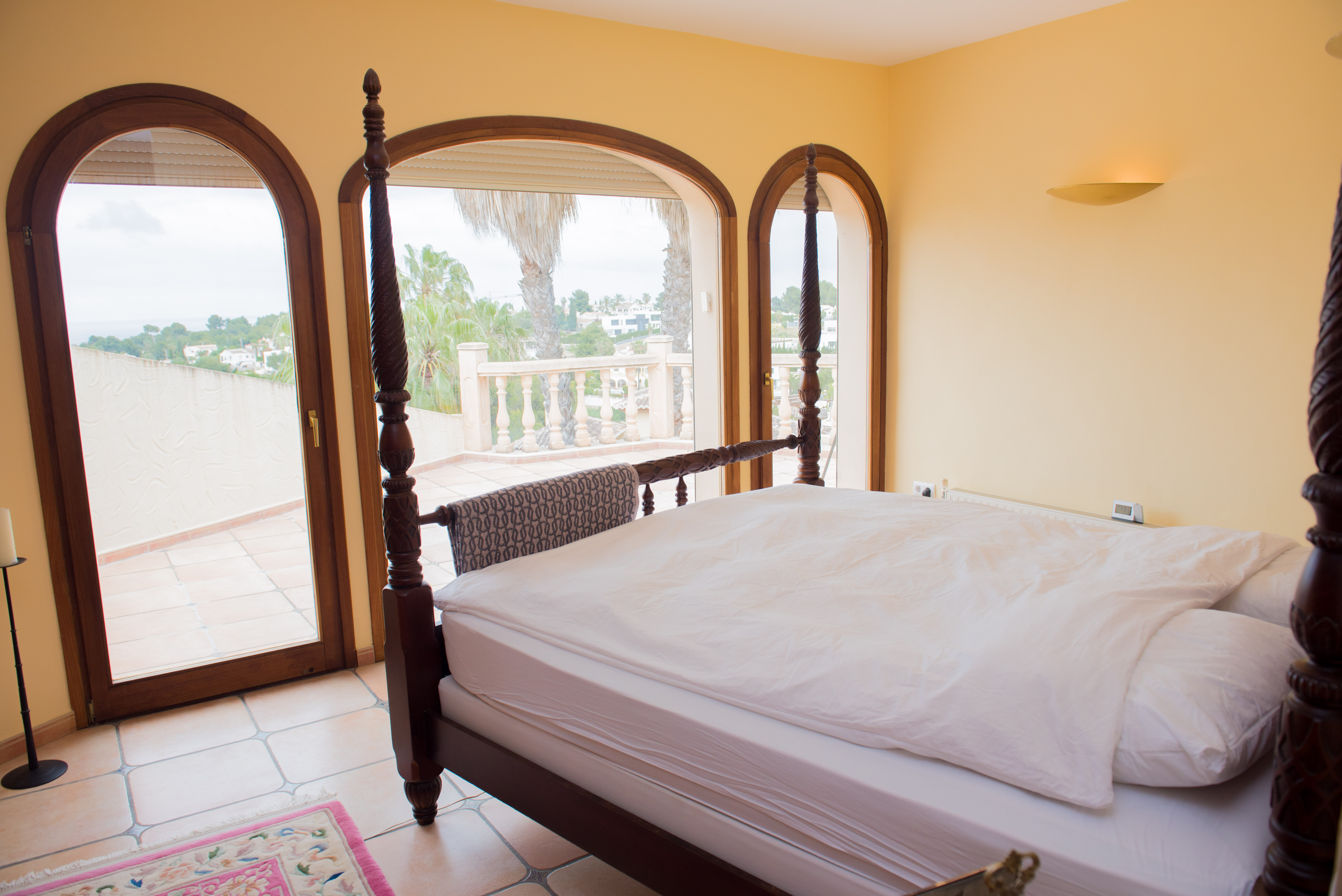Suite principal con cama de madera tallada y grandes ventanales de medio punto que ofrecen acceso directo a la terraza y vistas despejadas.