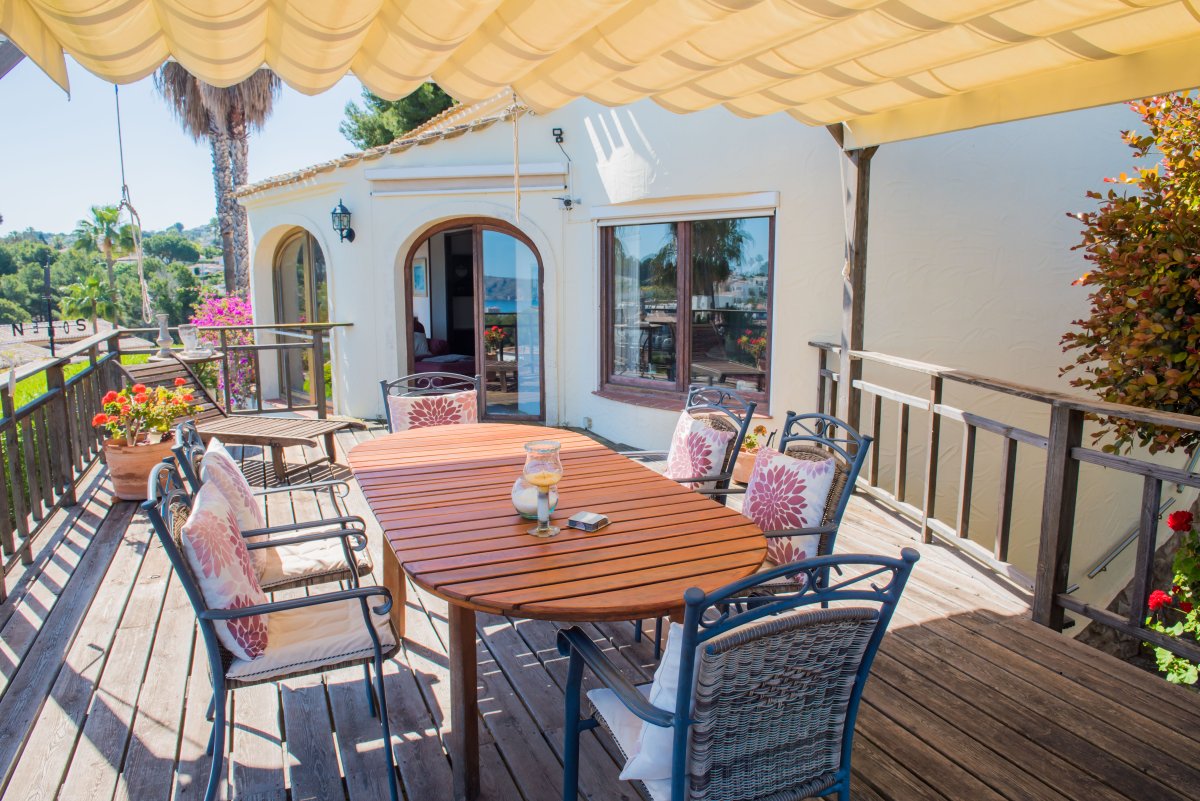 Terraza cubierta con mesa de madera y sillas tapizadas, ideal para disfrutar de vistas panorámicas al mar Mediterráneo.