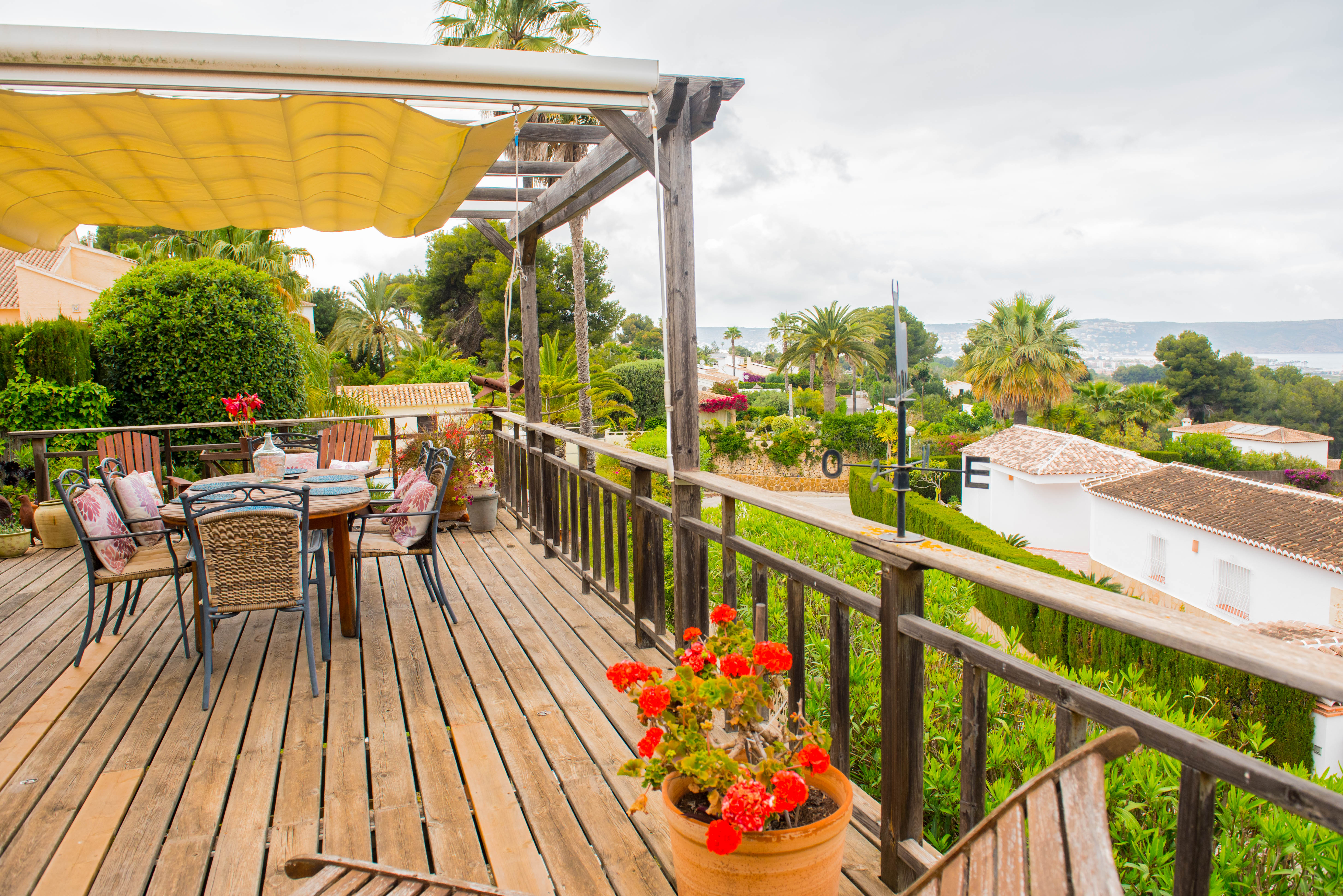 Terraza elevada de madera con toldo extensible, zona de comedor exterior y barandilla rústica con vistas panorámicas al mar y al entorno mediterráneo.