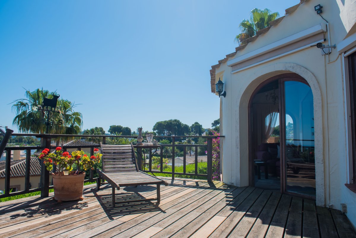 Terraza soleada con suelo de madera, tumbona y vistas al paisaje mediterráneo.