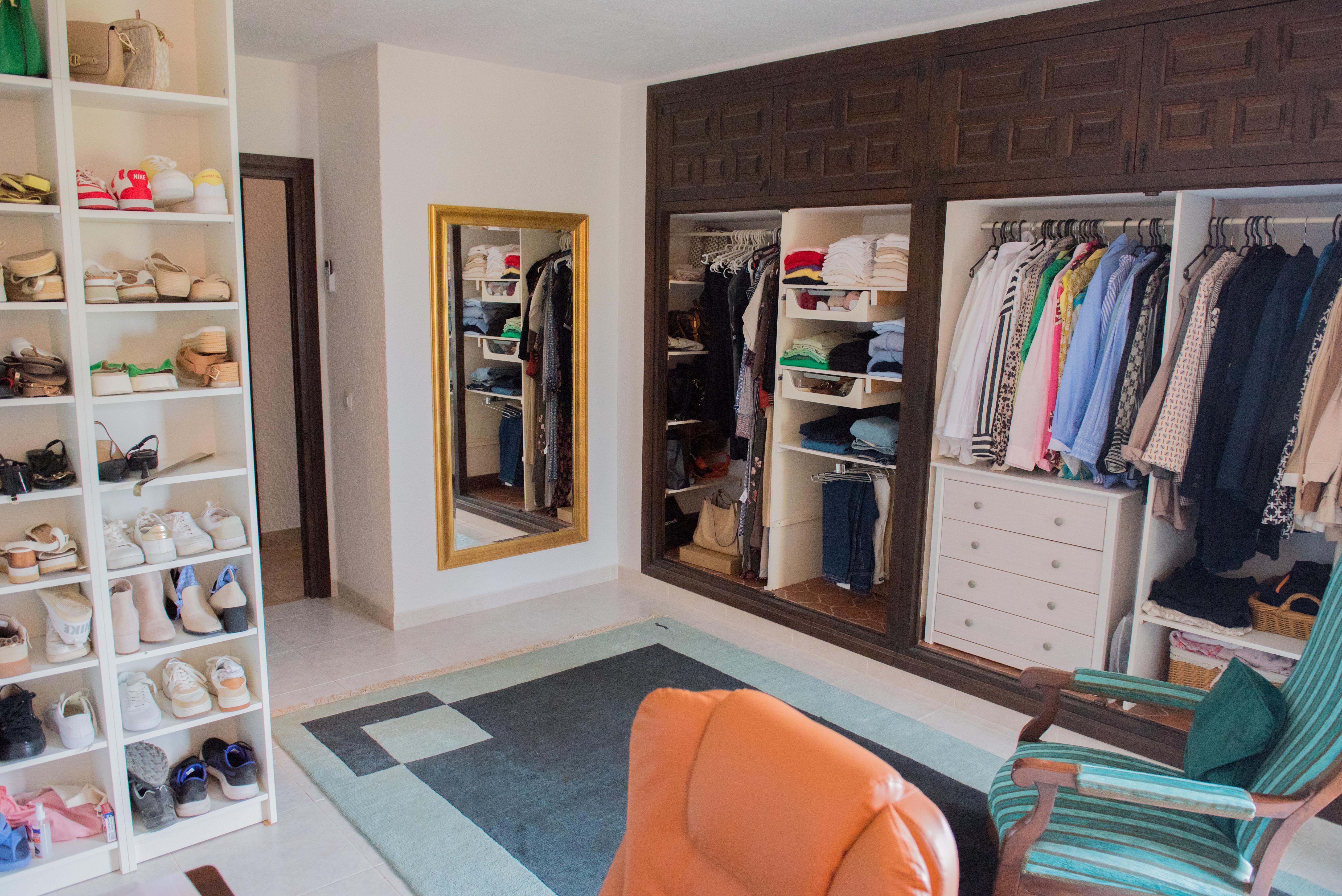 Vestidor espacioso con armarios empotrados de madera oscura, estanterías blancas para calzado, espejo de cuerpo entero con marco dorado y zona de estar con alfombra geométrica.