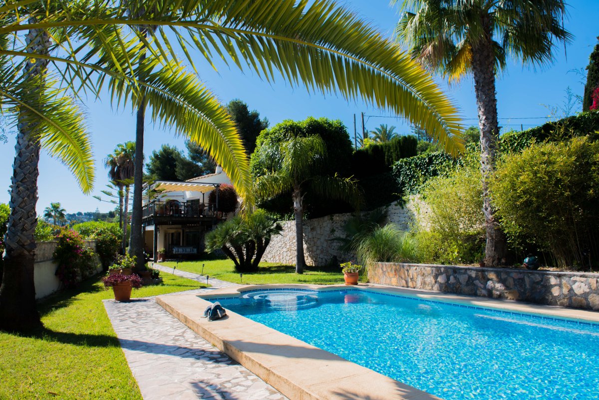 Vista de la piscina con mosaicos azules y jardín mediterráneo con palmeras en Jávea.