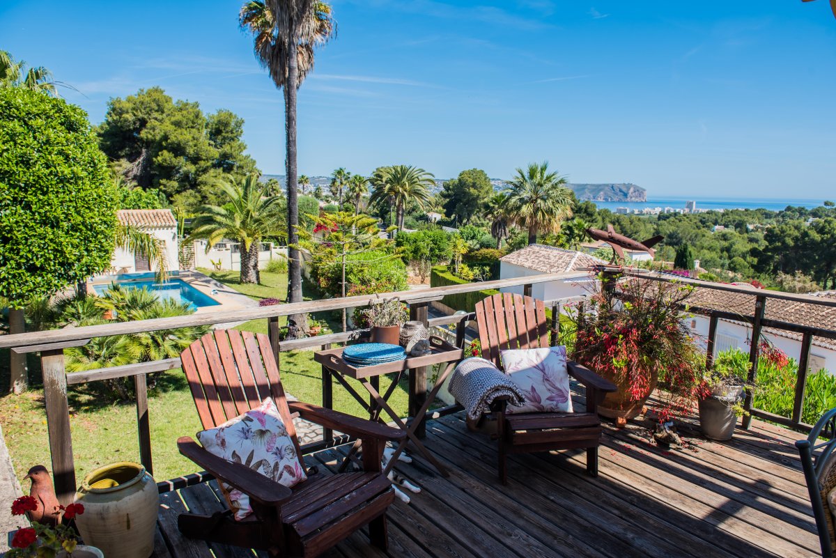 Vista desde la terraza de madera con sillas Adirondack, jardines y vistas panorámicas al mar en Jávea.