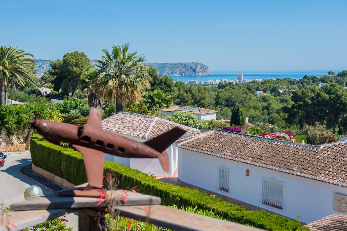 Vista panorámica de Jávea desde la terraza, con escultura de avión en primer plano y vegetación exuberante.