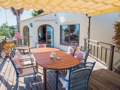 Terraza cubierta con mesa de madera y sillas tapizadas, ideal para disfrutar de vistas panorámicas al mar Mediterráneo.