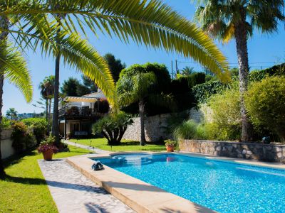 Vista de la piscina con mosaicos azules y jardín mediterráneo con palmeras en Jávea.