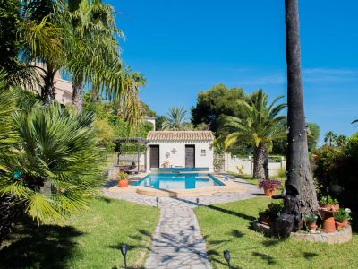Vista de la piscina de 8x4 m con bomba de calor, rodeada de jardines y una cocina de verano equipada en Jávea.