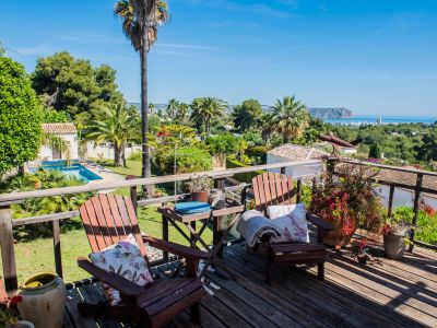 Vista desde la terraza de madera con sillas Adirondack, jardines y vistas panorámicas al mar en Jávea.