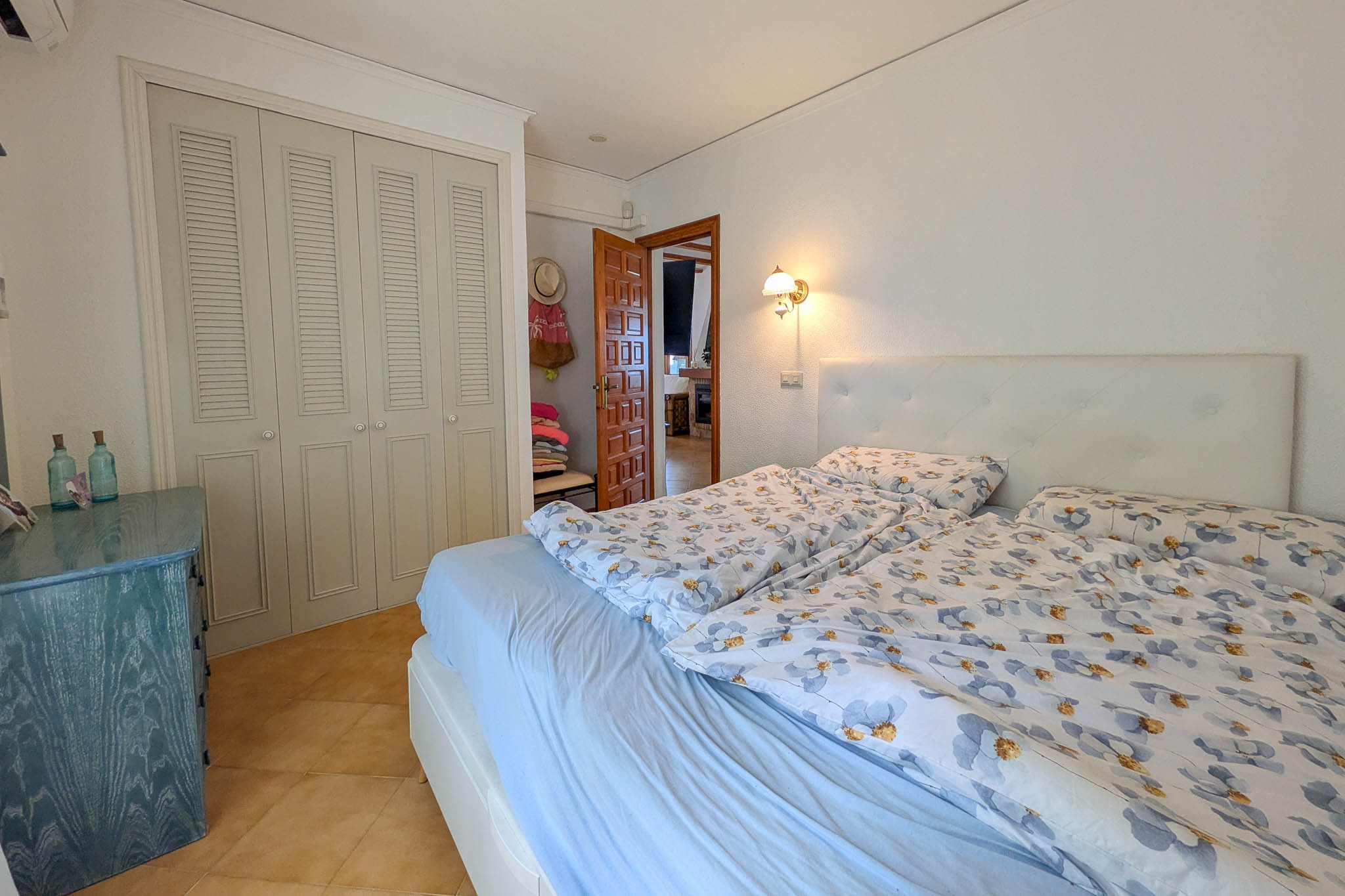 Dormitorio con armarios empotrados de puertas mallorquinas, suelos de gres cerámico y cabecero capitoné. Incluye una cómoda de madera azul y acceso directo al salón.