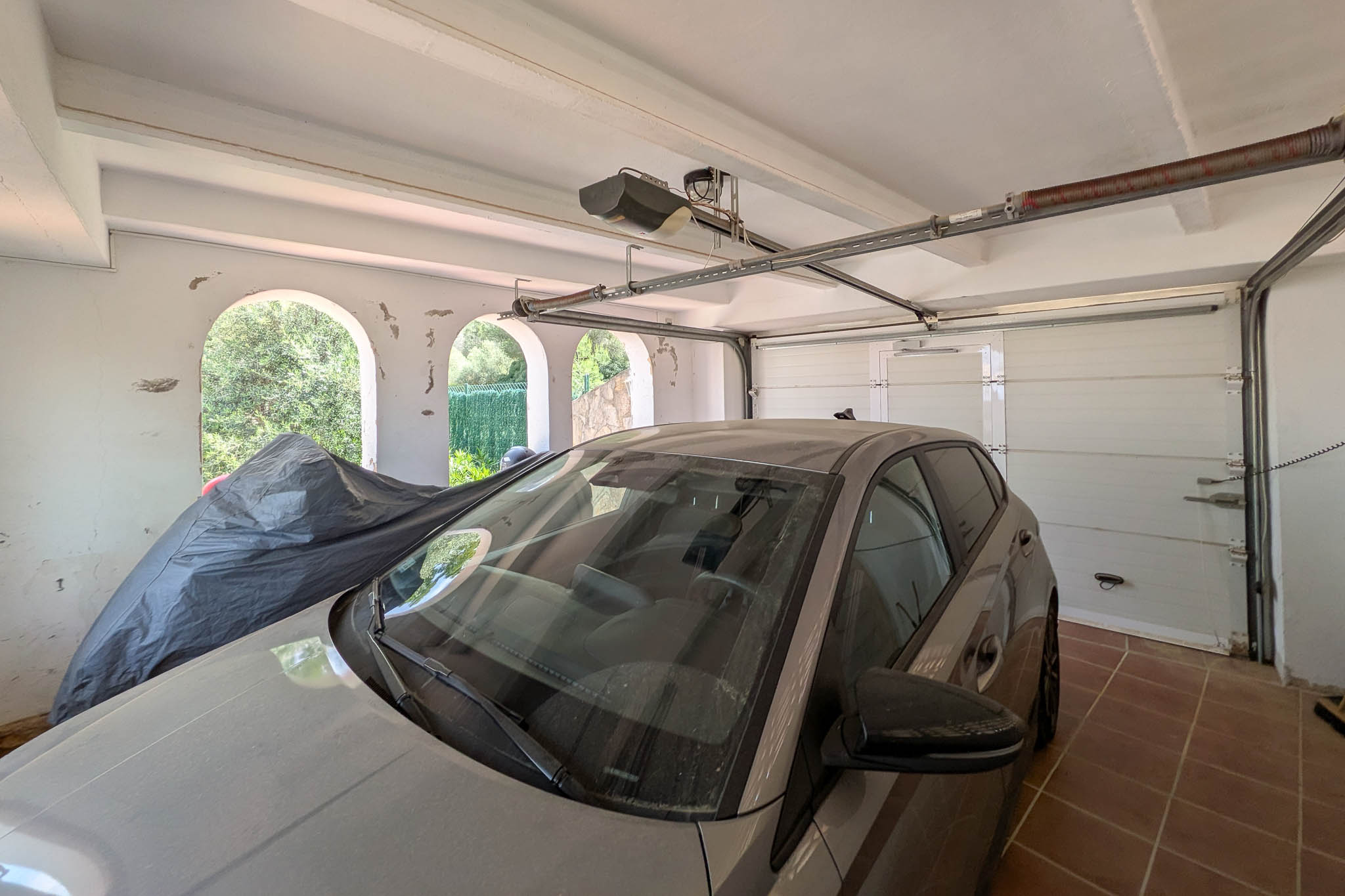 Garaje cerrado con puerta automática seccional, suelo de gres y techos con vigas. Las aperturas en arco integran luz natural y ventilación constante.