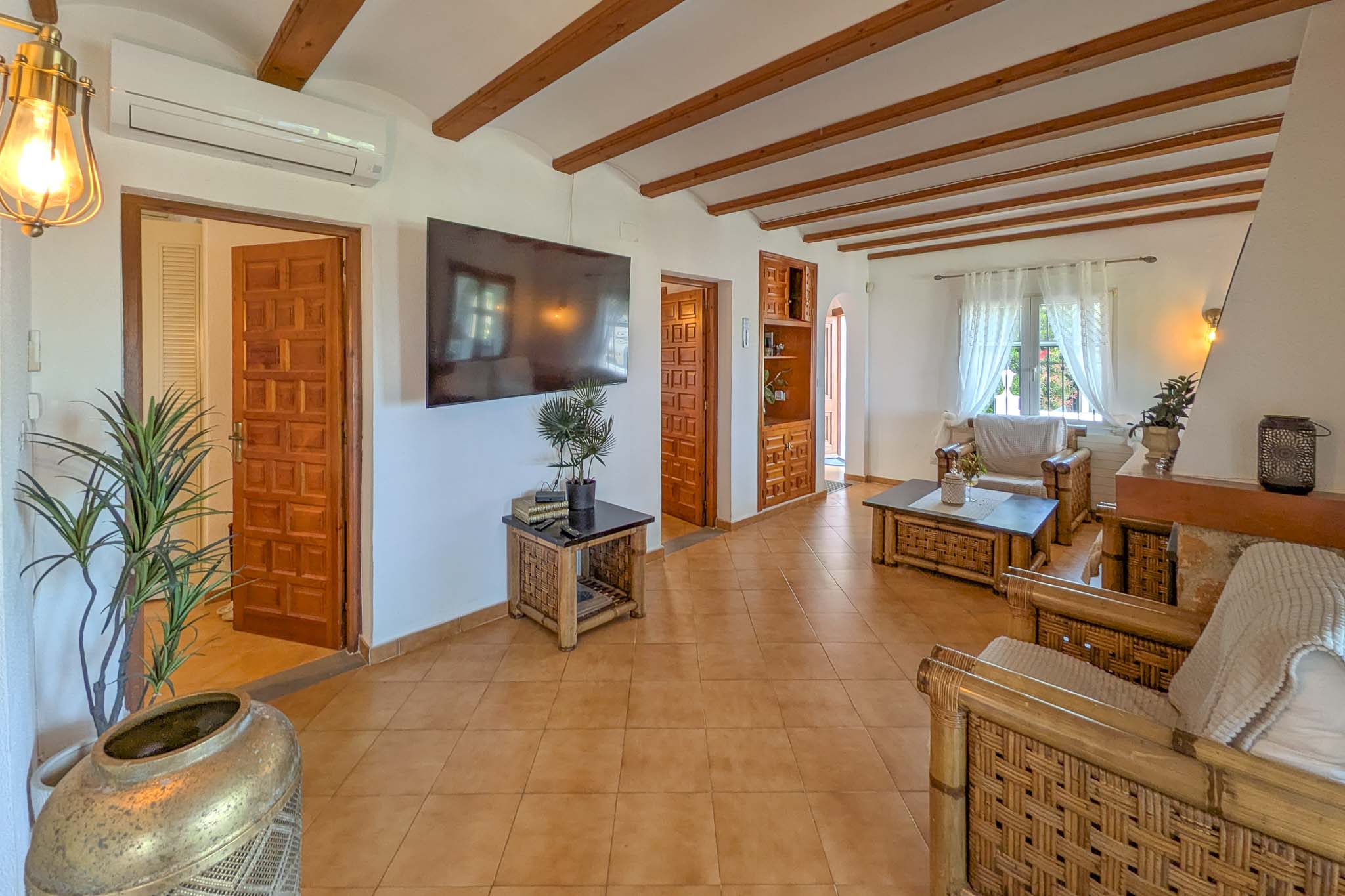 Salón rústico con vigas de madera vistas, suelos de terracota y mobiliario de bambú. Incluye aire acondicionado y acceso a estancias mediante puertas de madera labrada.
