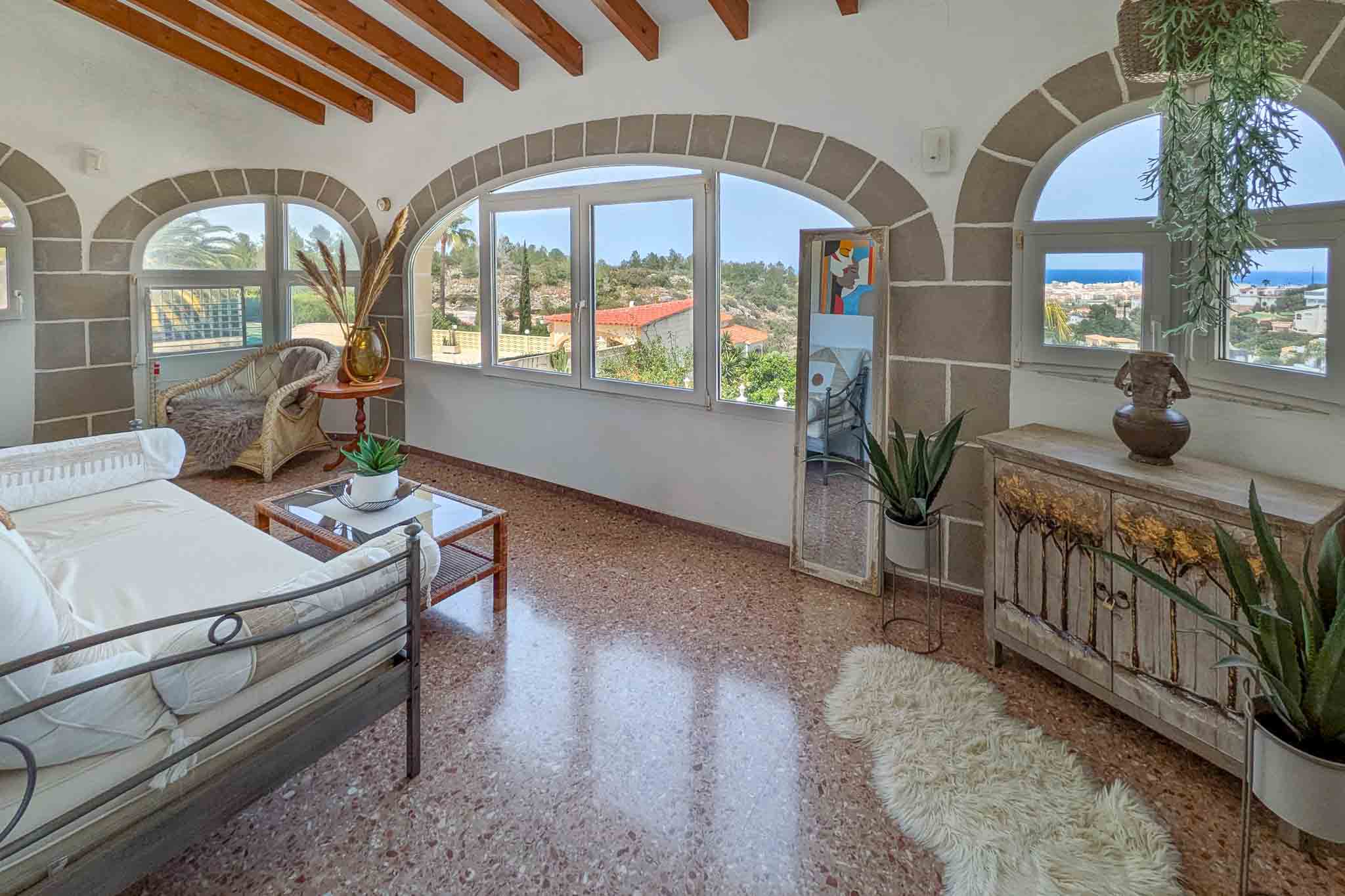 Terraza acristalada con arcos de piedra, vigas de madera y suelo de terrazo. Ofrece vistas panorámicas al mar Mediterráneo y al entorno natural de Dénia.