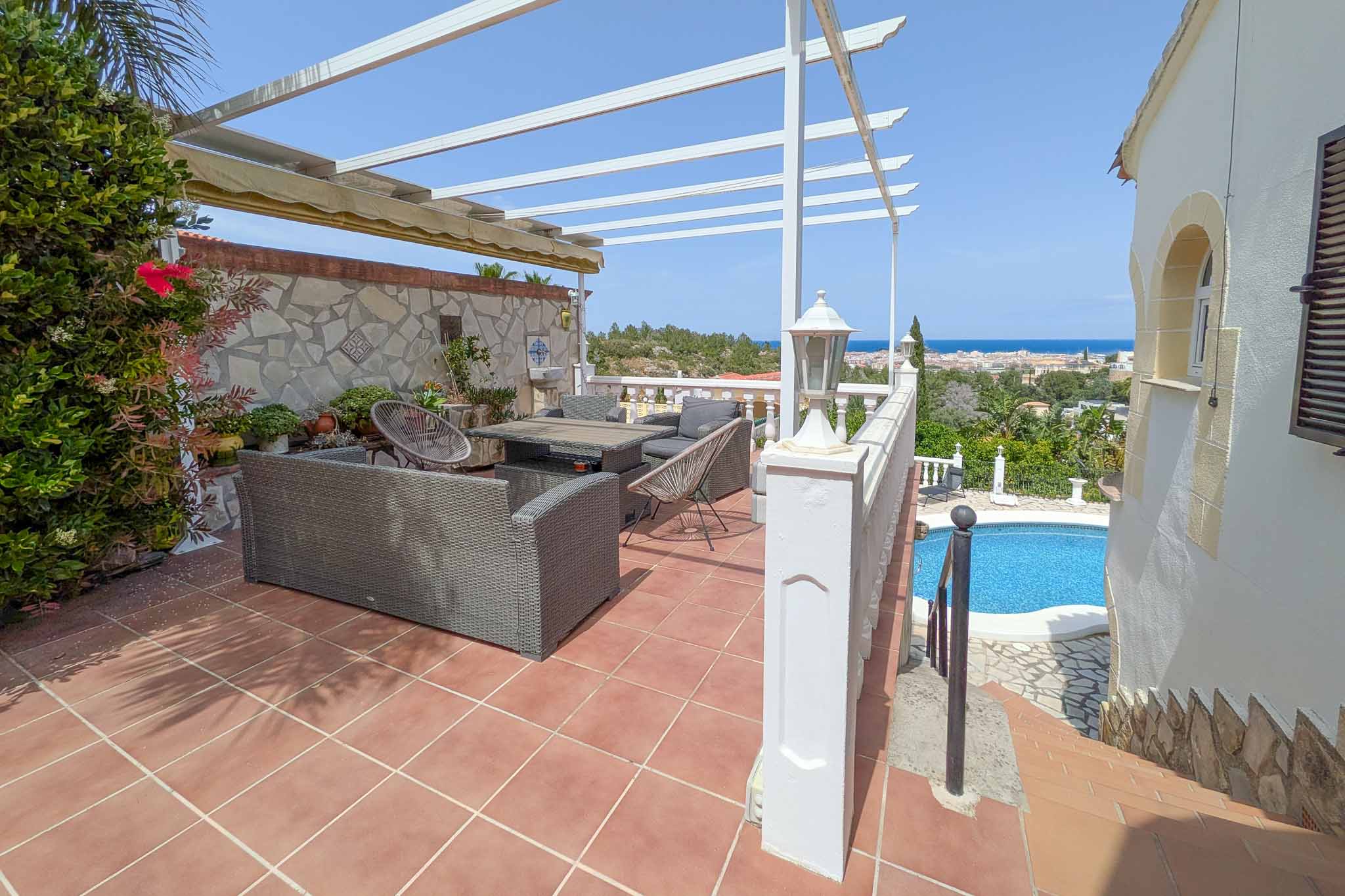 Terraza superior con zona de estar exterior, pérgola blanca y vistas panorámicas al mar Mediterráneo y Dénia, situada sobre el nivel de la piscina.