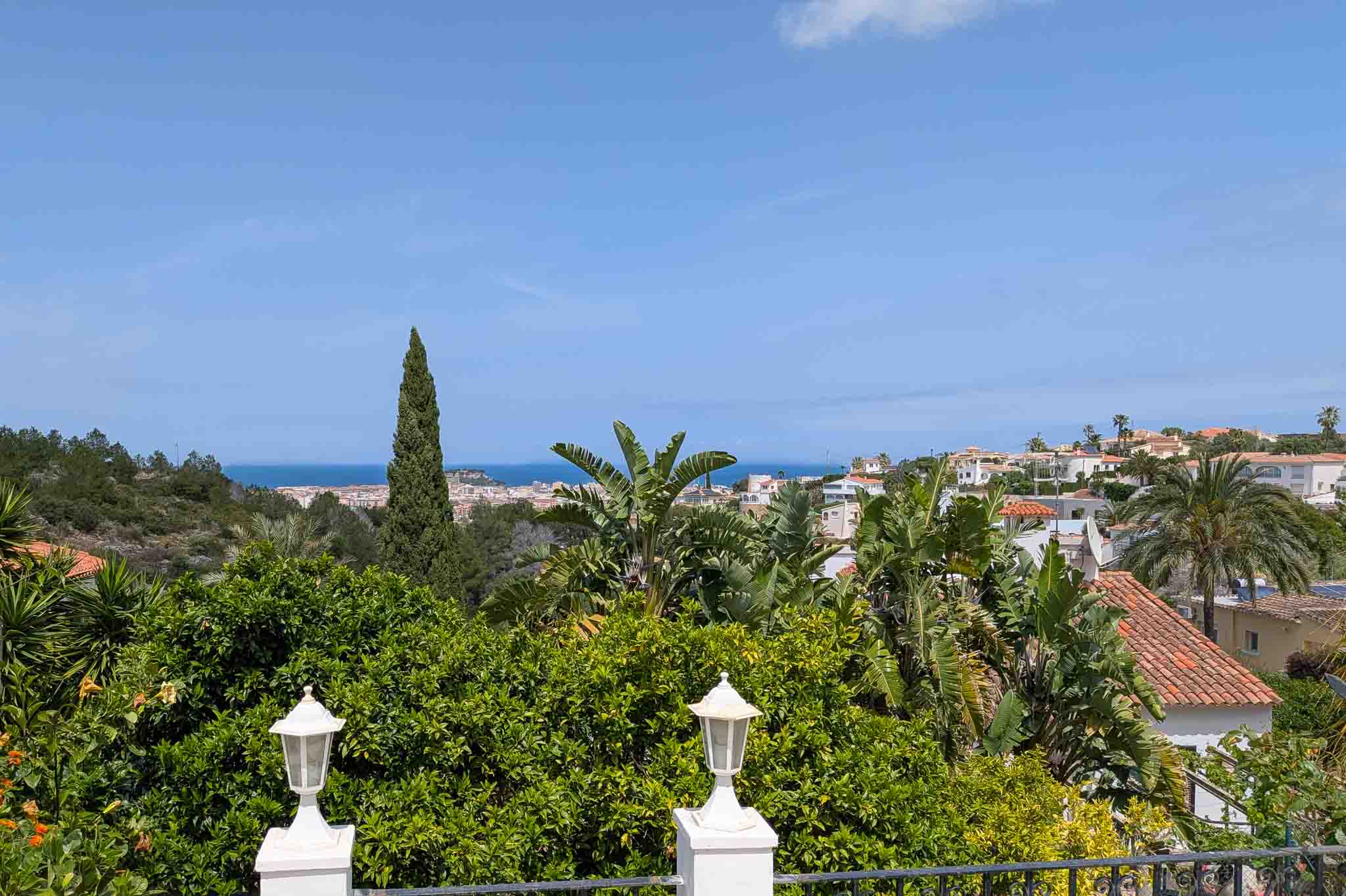 Vistas panorámicas al mar y al casco urbano de Dénia desde la terraza superior, enmarcada por vegetación mediterránea y cítricos.
