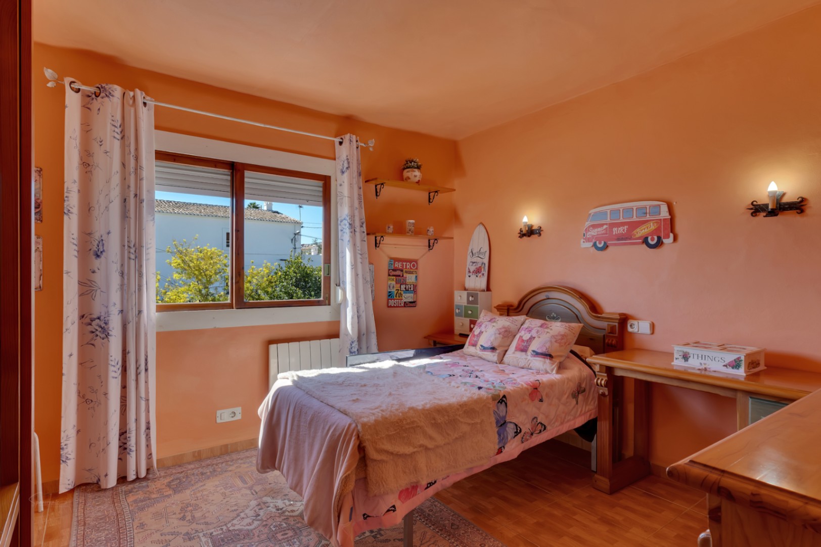 Dormitorio luminoso con paredes en tono salmón, cama individual, escritorio de madera y ventana al exterior. Incluye calefacción por radiador y suelos cerámicos.