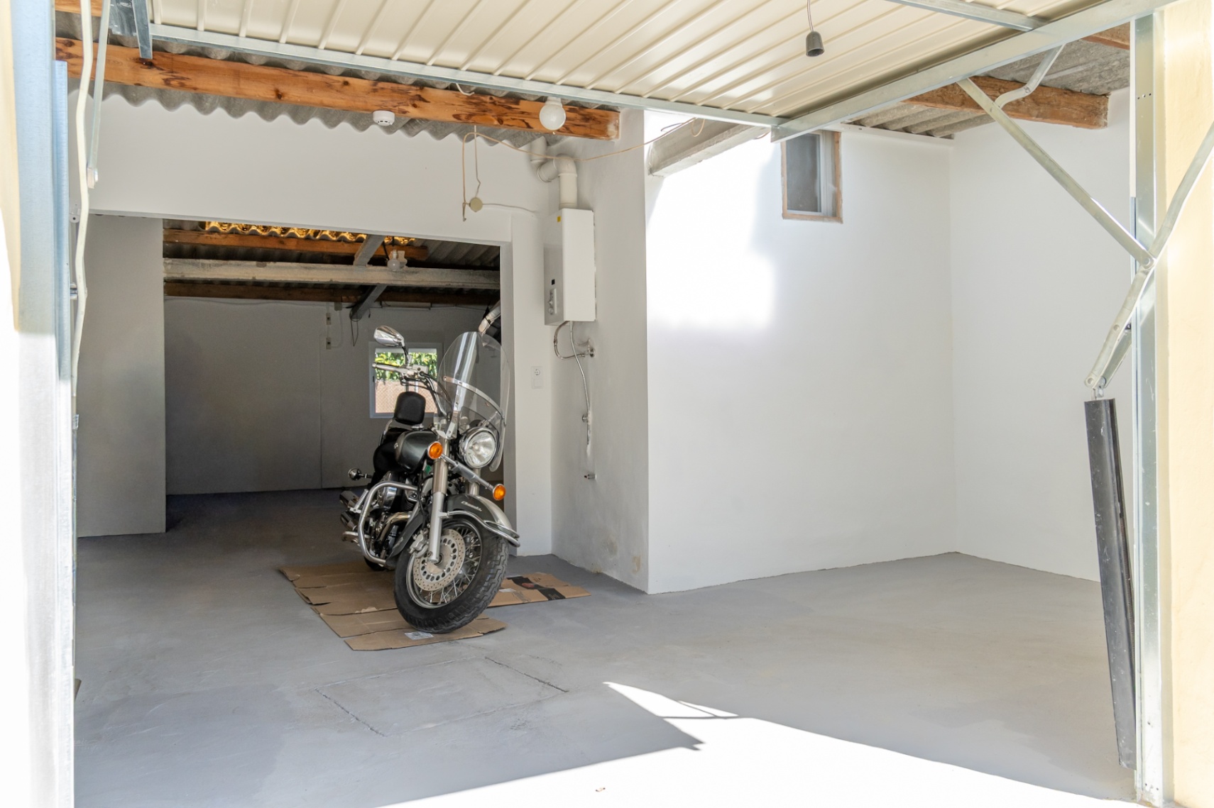 Garaje cerrado y zona de aparcamiento con suelos de hormigón, techos de vigas de madera y calentador de gas instalado, ideal para vehículos y almacenamiento.