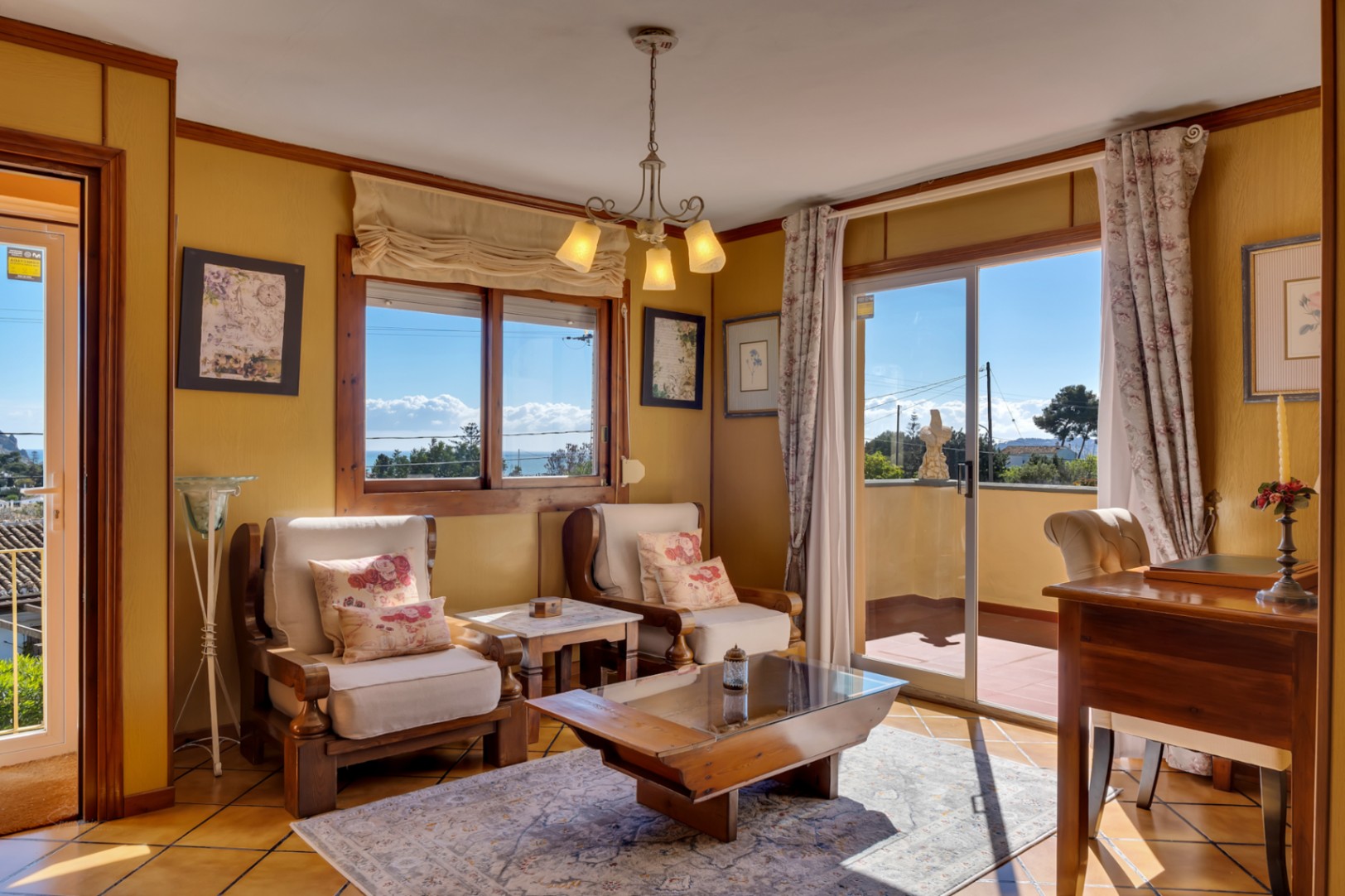 Sala de estar luminosa con mobiliario de madera, suelos de baldosa y acceso directo a una terraza con vistas al mar Mediterráneo.