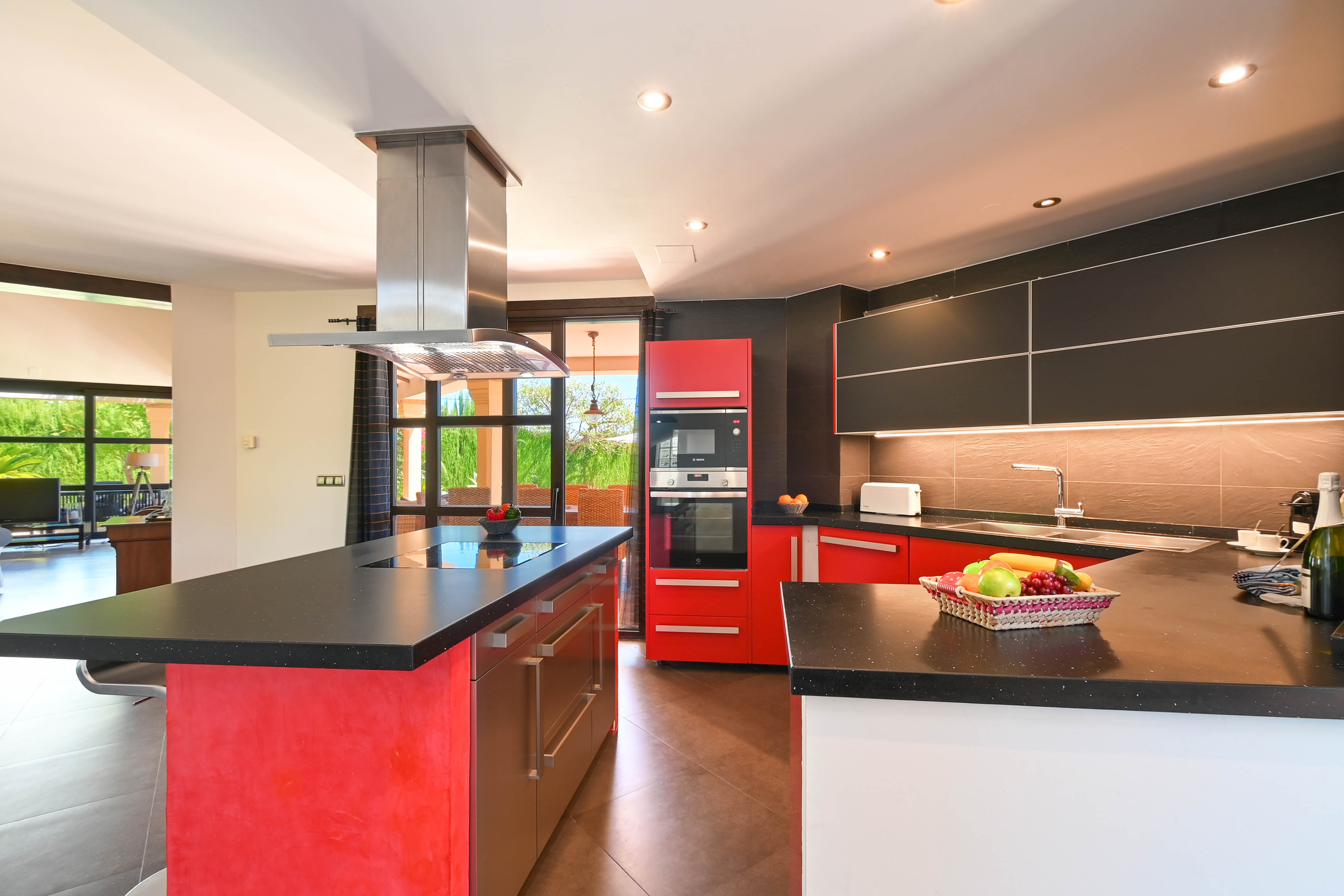 Cocina moderna con encimeras de granito negro, armarios rojos y negros, y electrodomésticos de acero inoxidable.