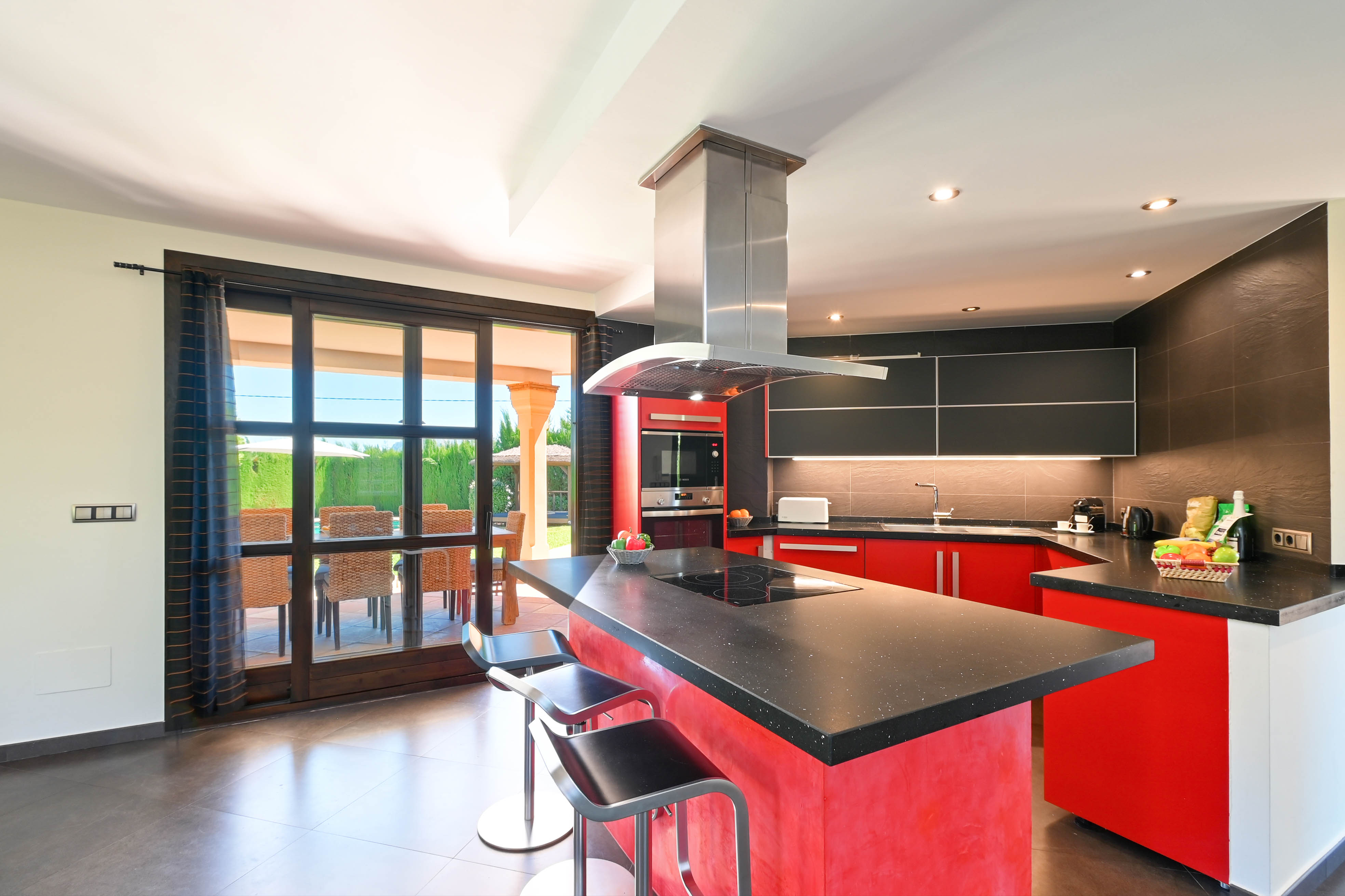 Cocina moderna con isla central, encimera de granito negro y taburetes metálicos.