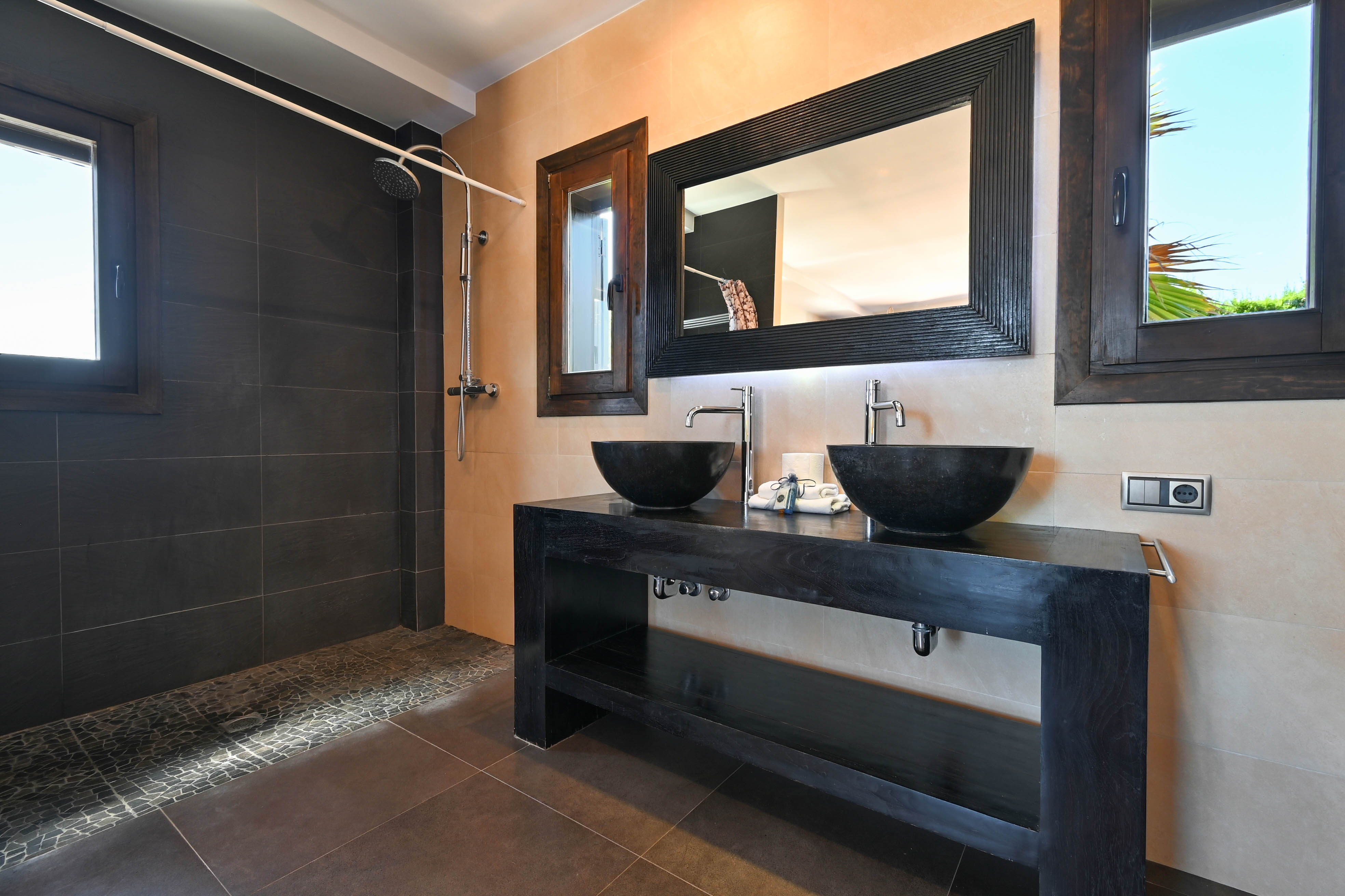 Detalle de baño moderno con lavabo doble de piedra y ducha con azulejos oscuros.
