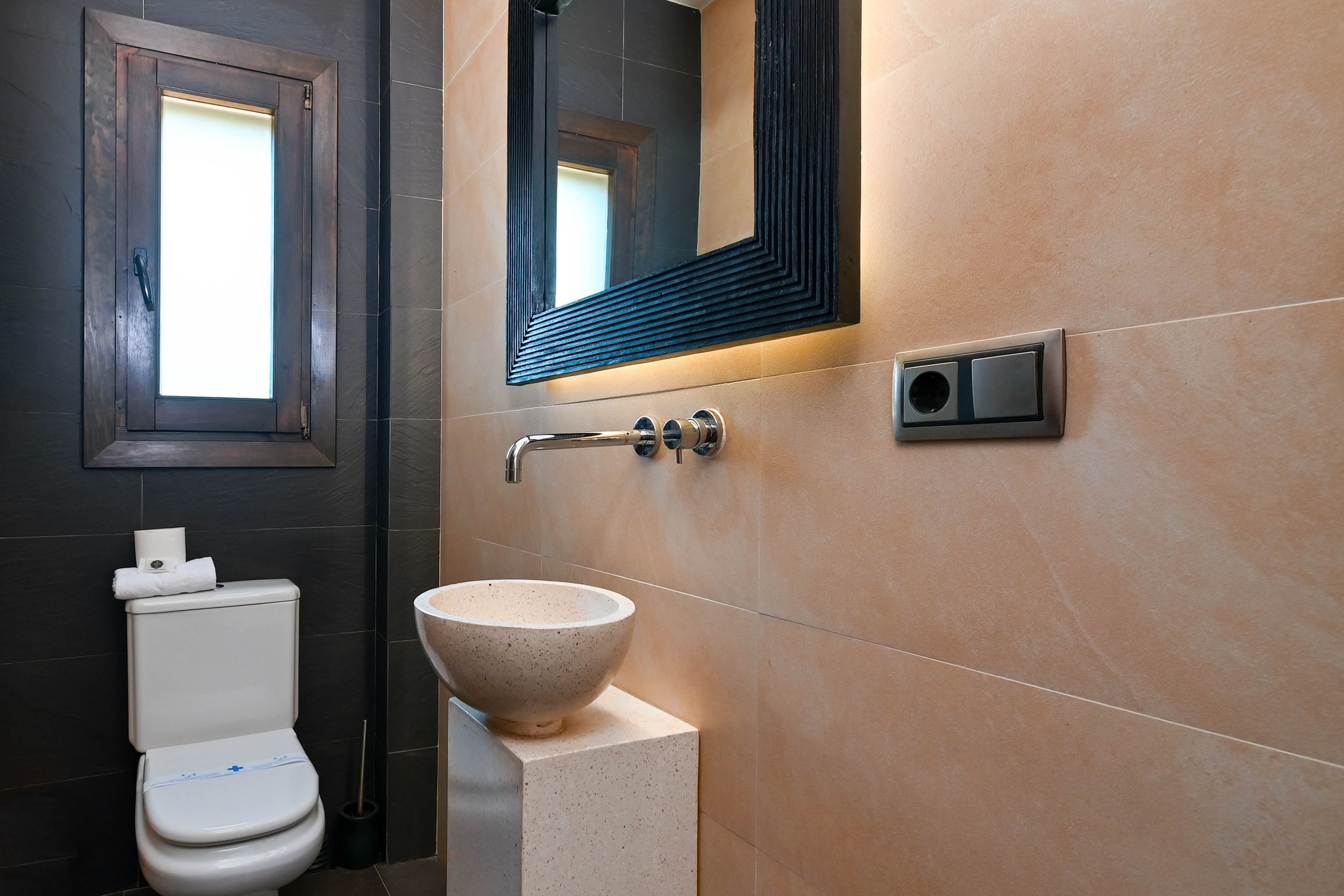 Detalle de baño moderno con lavabo esférico de piedra y espejo con iluminación integrada.