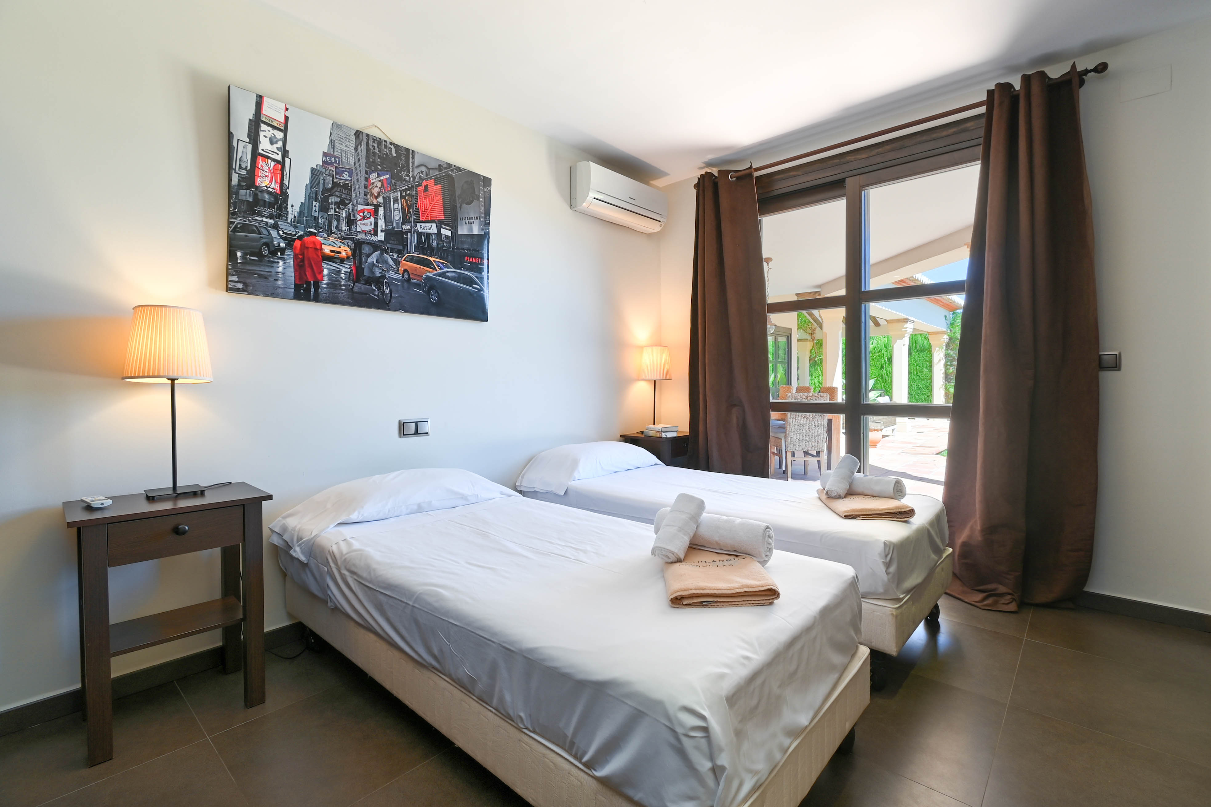 Dormitorio luminoso con dos camas individuales, mesita de noche de madera oscura y decoración moderna.