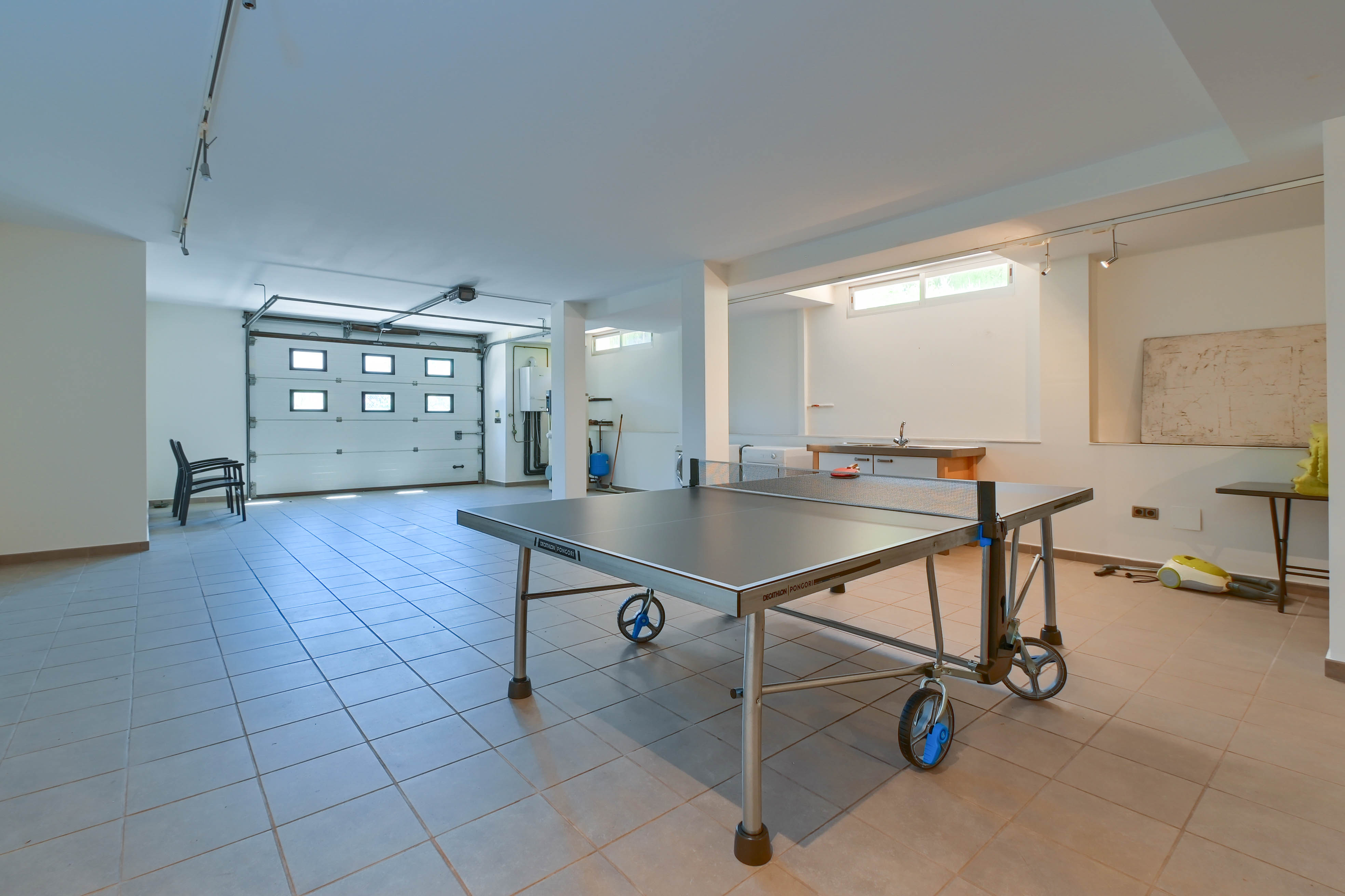Espacio de ocio con mesa de ping-pong Decathlon Pongori, suelo de baldosas y acceso al garaje.