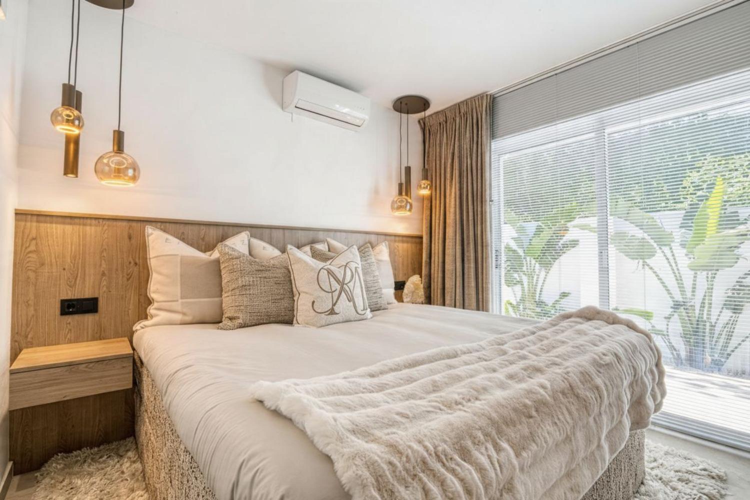 Dormitorio con cabecero de madera, lámparas colgantes de cristal y cortinas beige junto a la ventana.