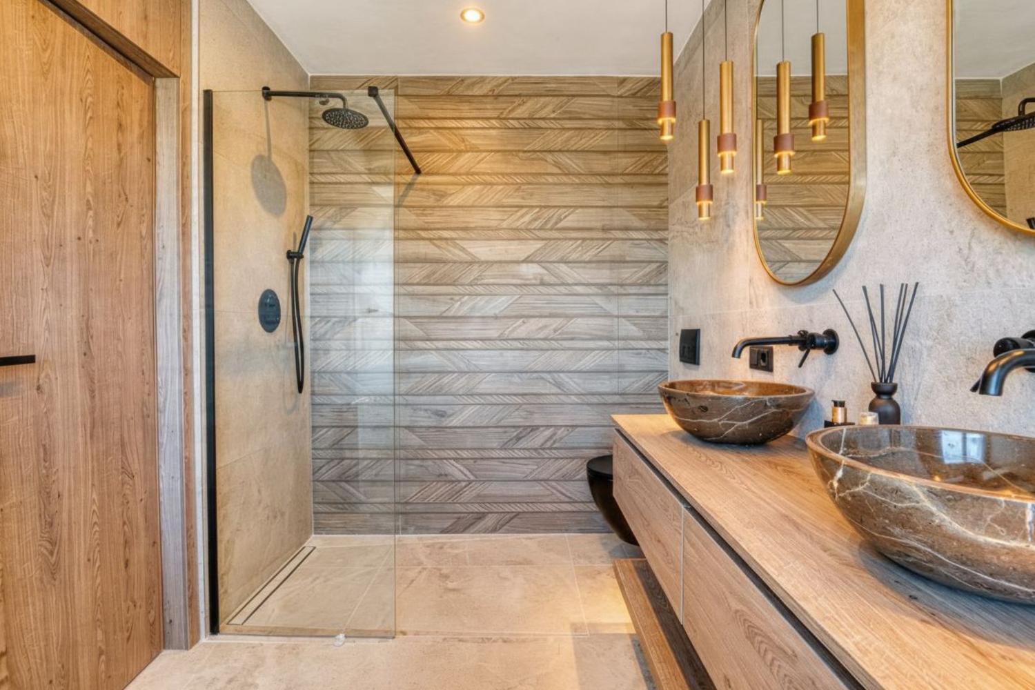 Elegante baño con lavabos de piedra y ducha con mampara de cristal, destacando el revestimiento de pared con diseño geométrico.