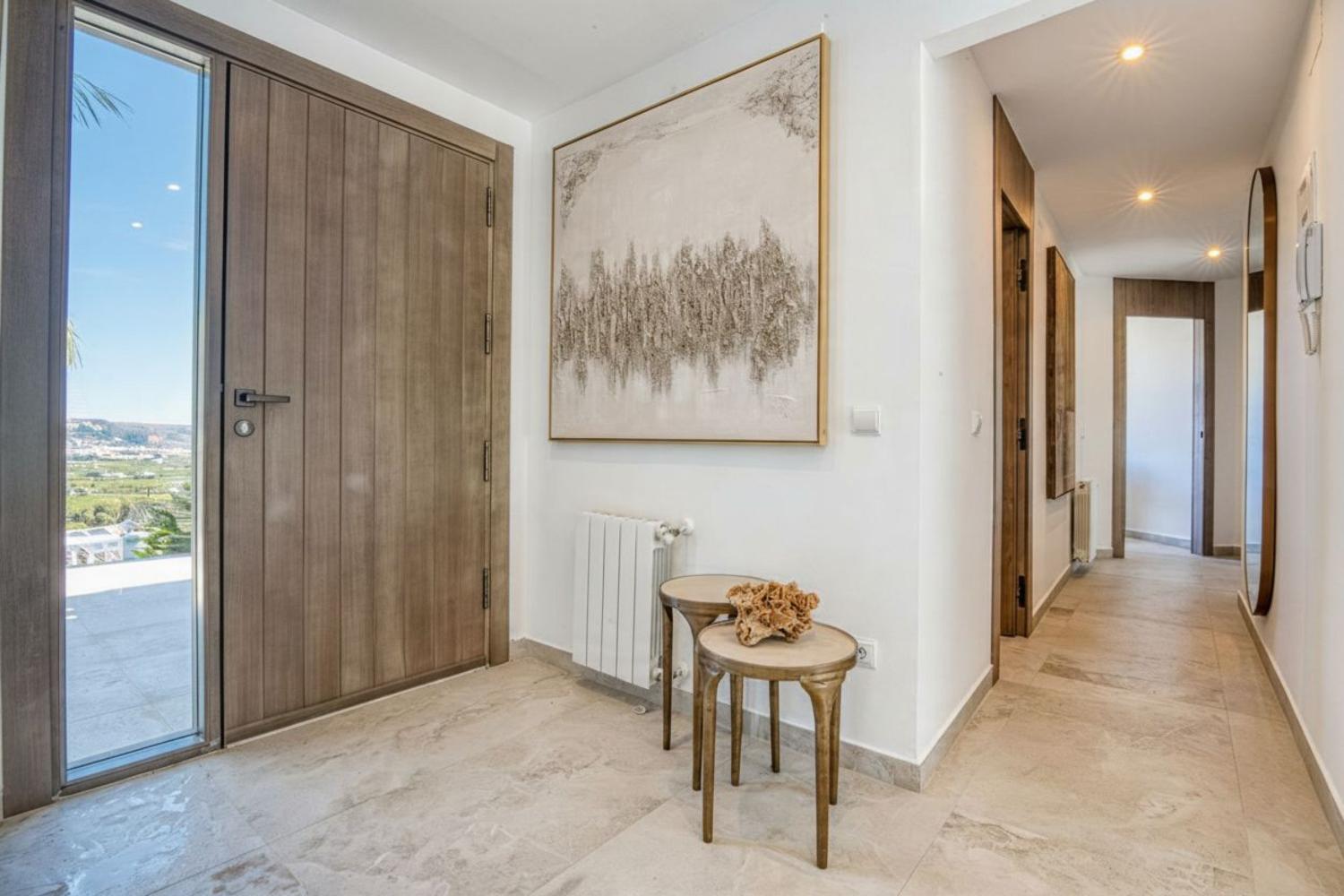 Entrada luminosa con puerta de madera y suelo de mármol. Detalle de obra de arte abstracta y mesas auxiliares.