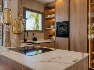 Detalle de la cocina con isla de mármol veteado, armarios de madera clara y electrodomésticos modernos.